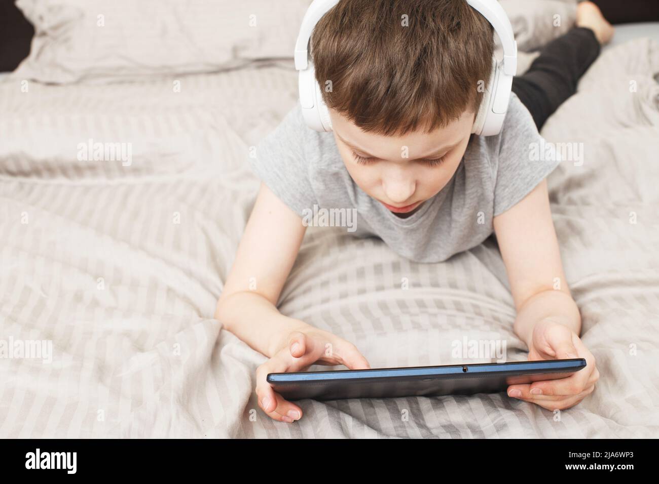 bambino che si trova a casa con un tablet pc e legge online, impara o ascolta musica con le cuffie wireless Foto Stock