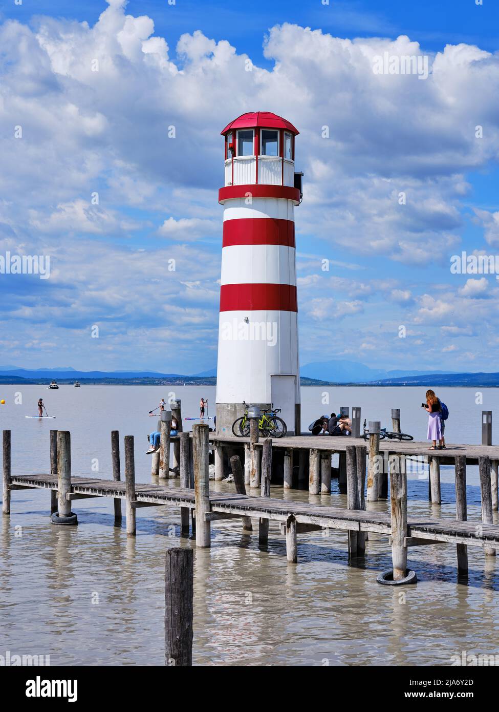 Faro rosso e bianco a Podersdorf am SEE, Austria, con molo in legno, lago Neusiedl e nuvoloso cielo estivo. Foto Stock