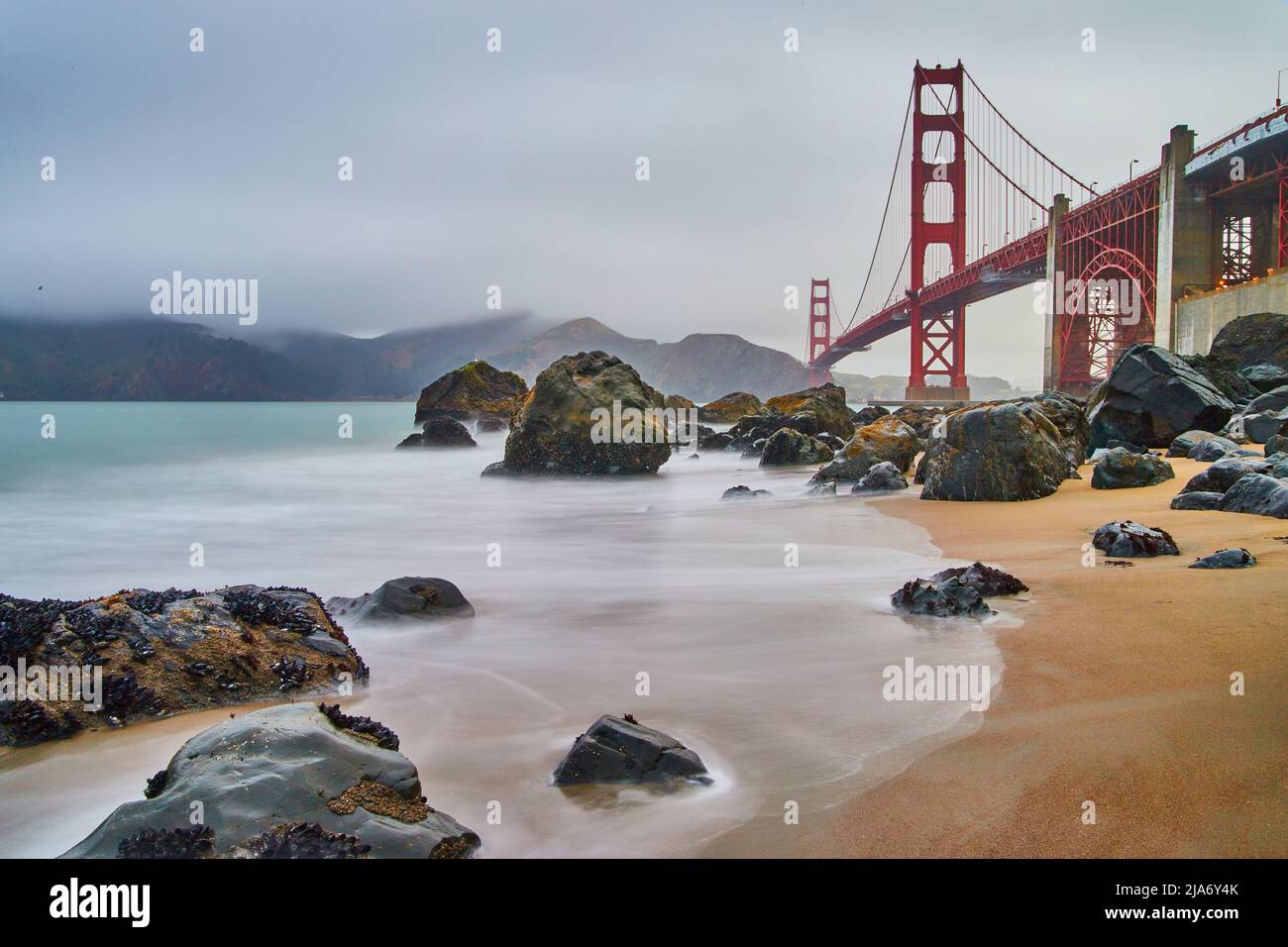 Ondate d'acqua sfocate che colpiscono la spiaggia sabbiosa e rocciosa a sud-ovest del Golden Gate Bridge Foto Stock