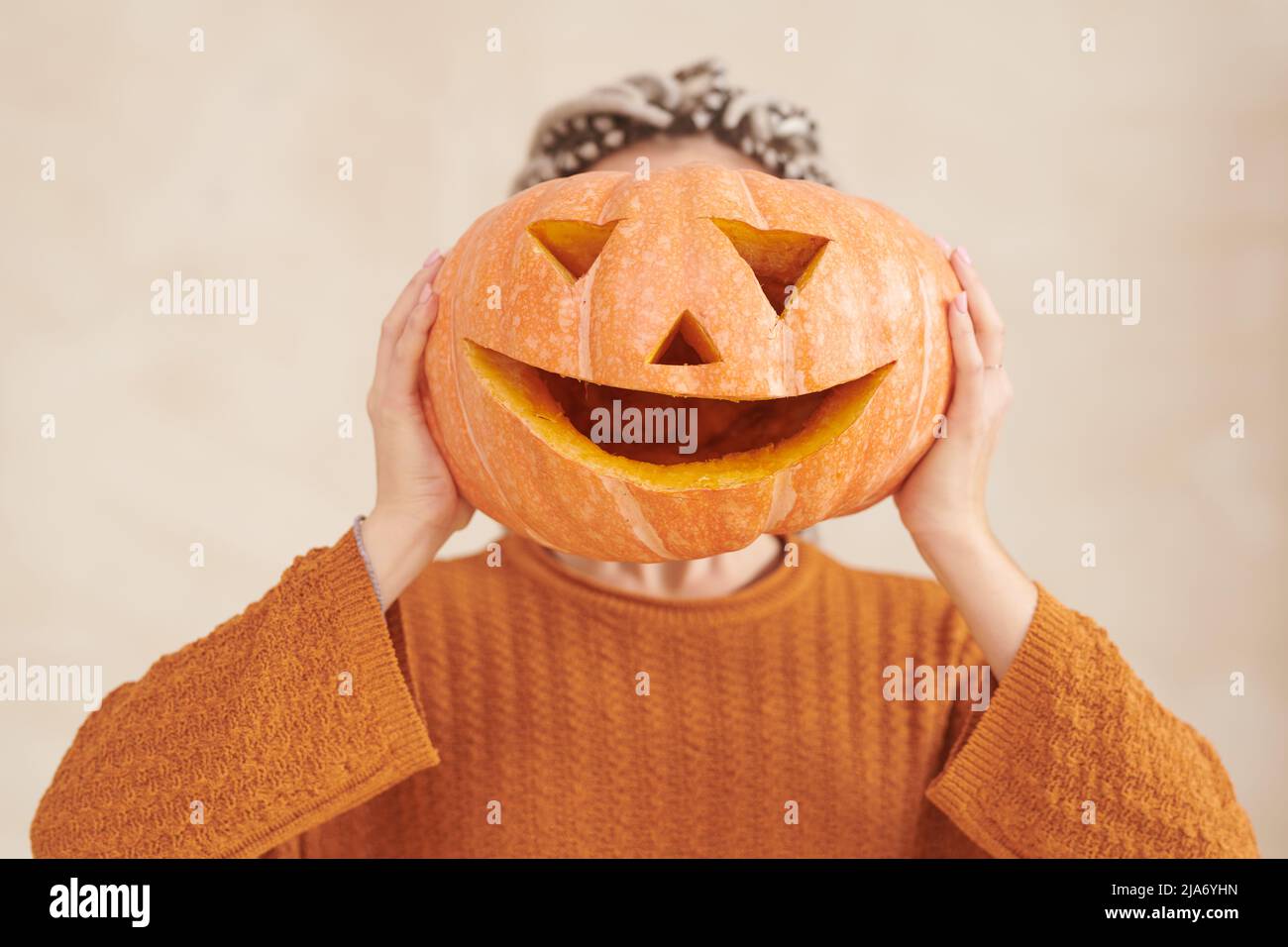 Donna irriconoscibile in maglione marrone che tiene divertente zucca contro faccia Halloween partito Foto Stock