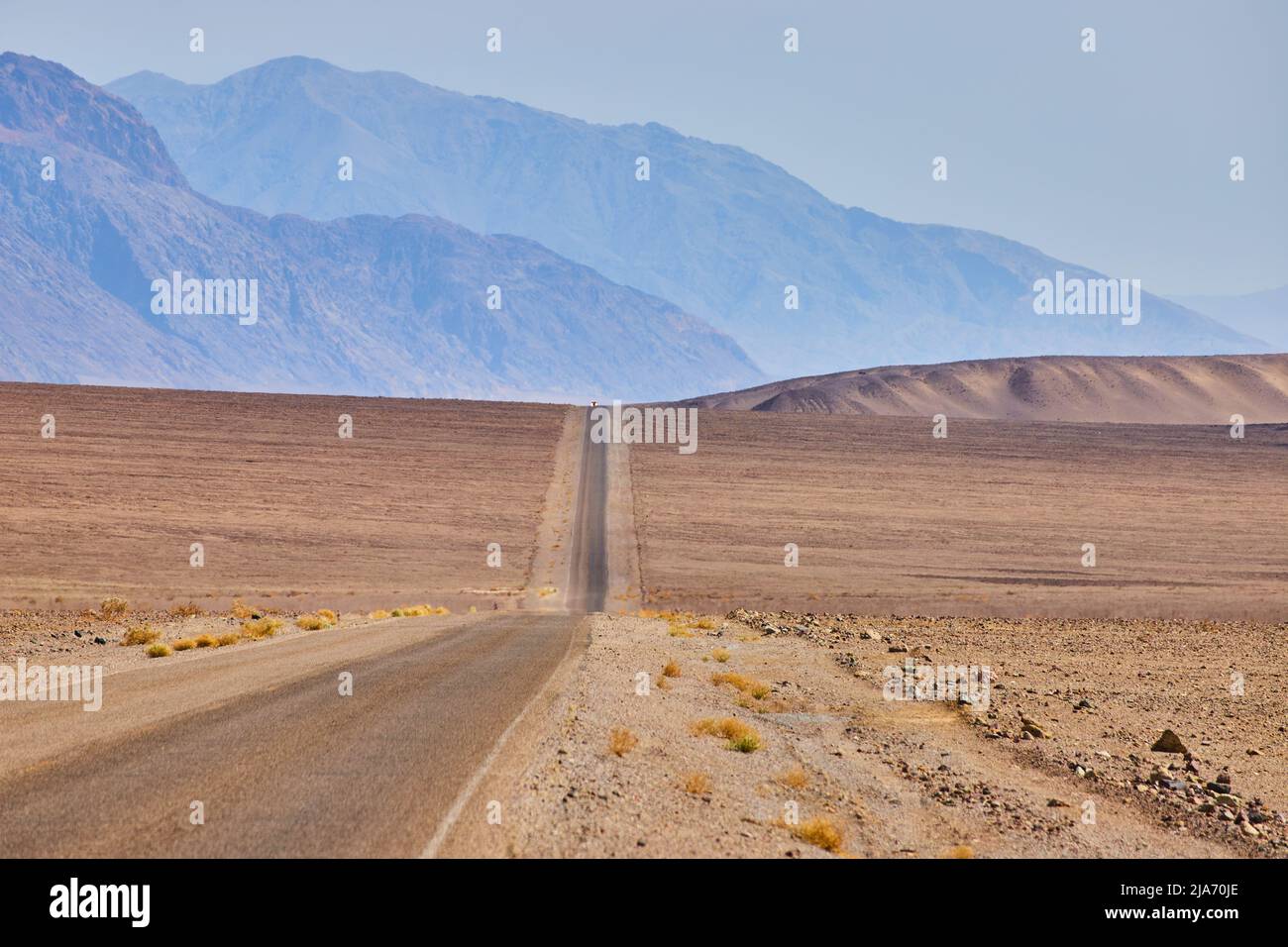 Strada del deserto che attraversa colline e pianure vuote che conducono alle montagne Foto Stock
