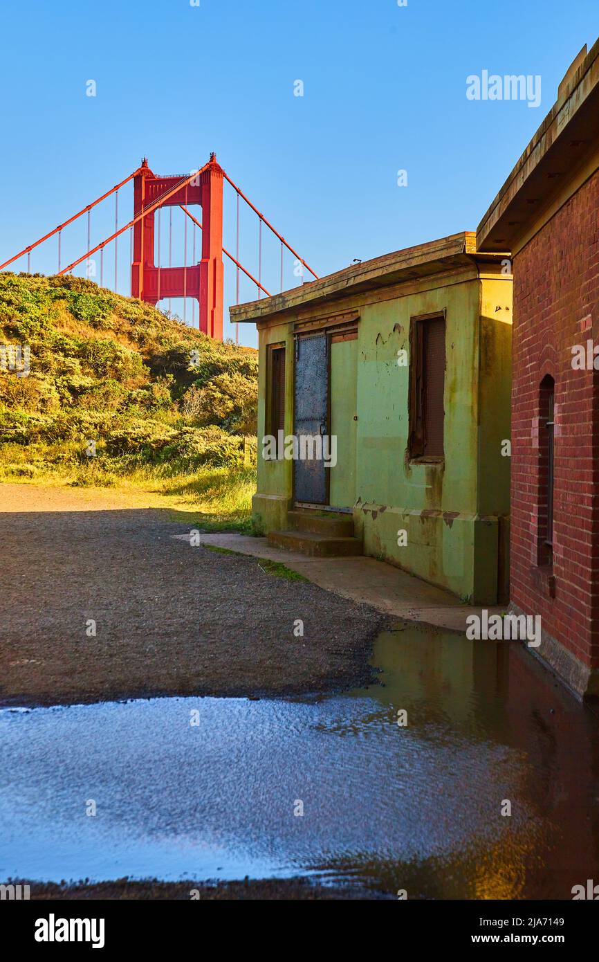 Golden Gate Bridge che si sbucciano sulle colline da un sentiero fiancheggiato da vecchie strutture Foto Stock