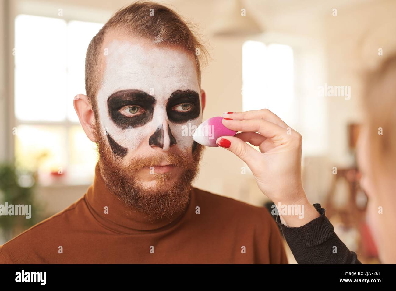 Primo piano di un irriconoscibile make-artist utilizzando spugna mentre si fa uomo viso bianco per Halloween partito Foto Stock