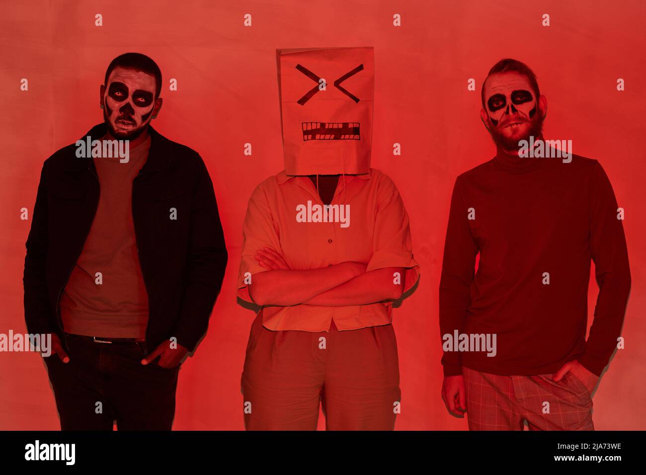 Gruppo di giovani amici con makeup terrificanti e persona con viso dispiaciuto su sacchetto di carta in piedi in linea, effetto luce rossa Foto Stock