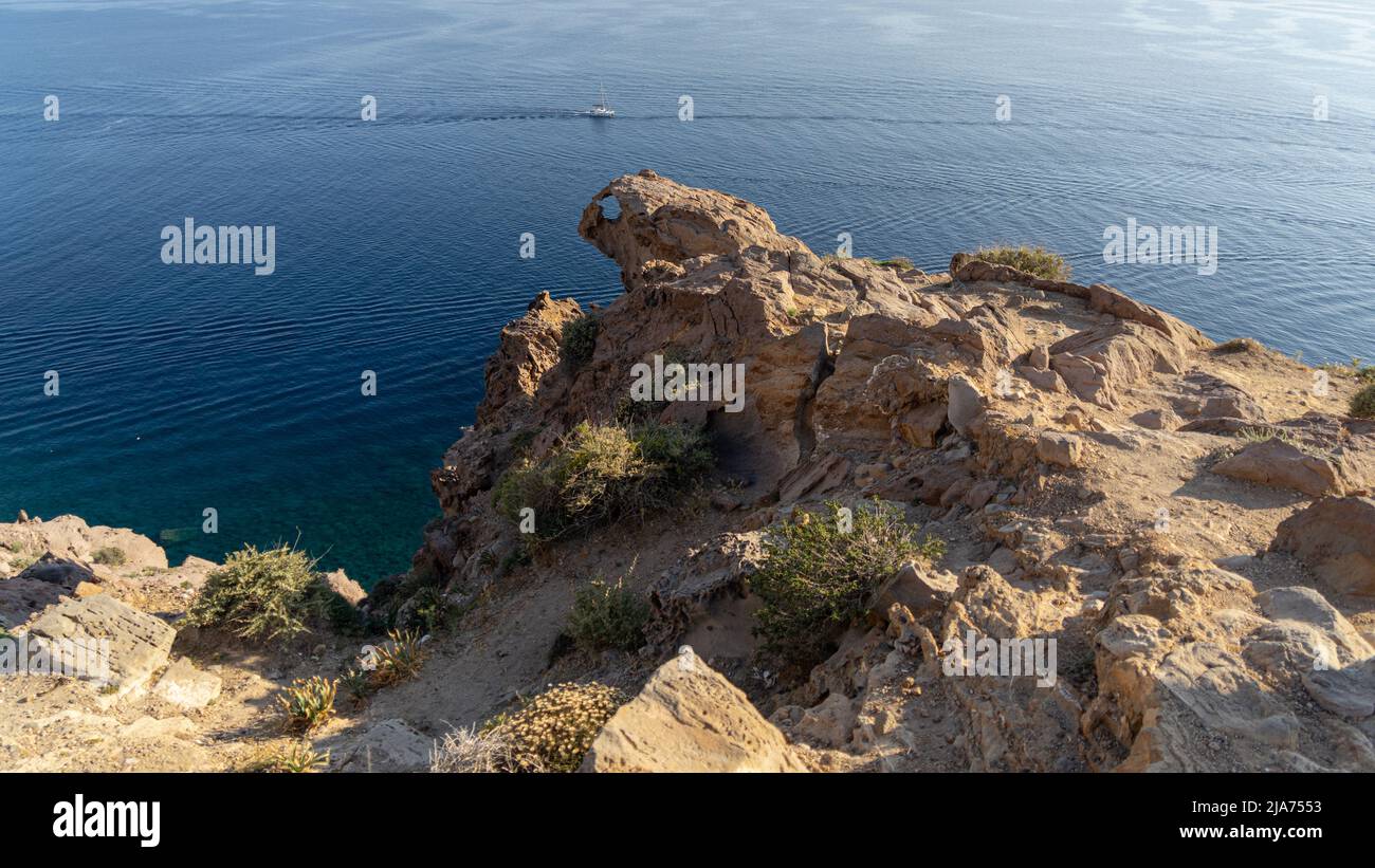 Santorini: Un promontorio roccioso sulla costa assomiglia alla testa di un drago che si schiaccia alle barche sotto Foto Stock