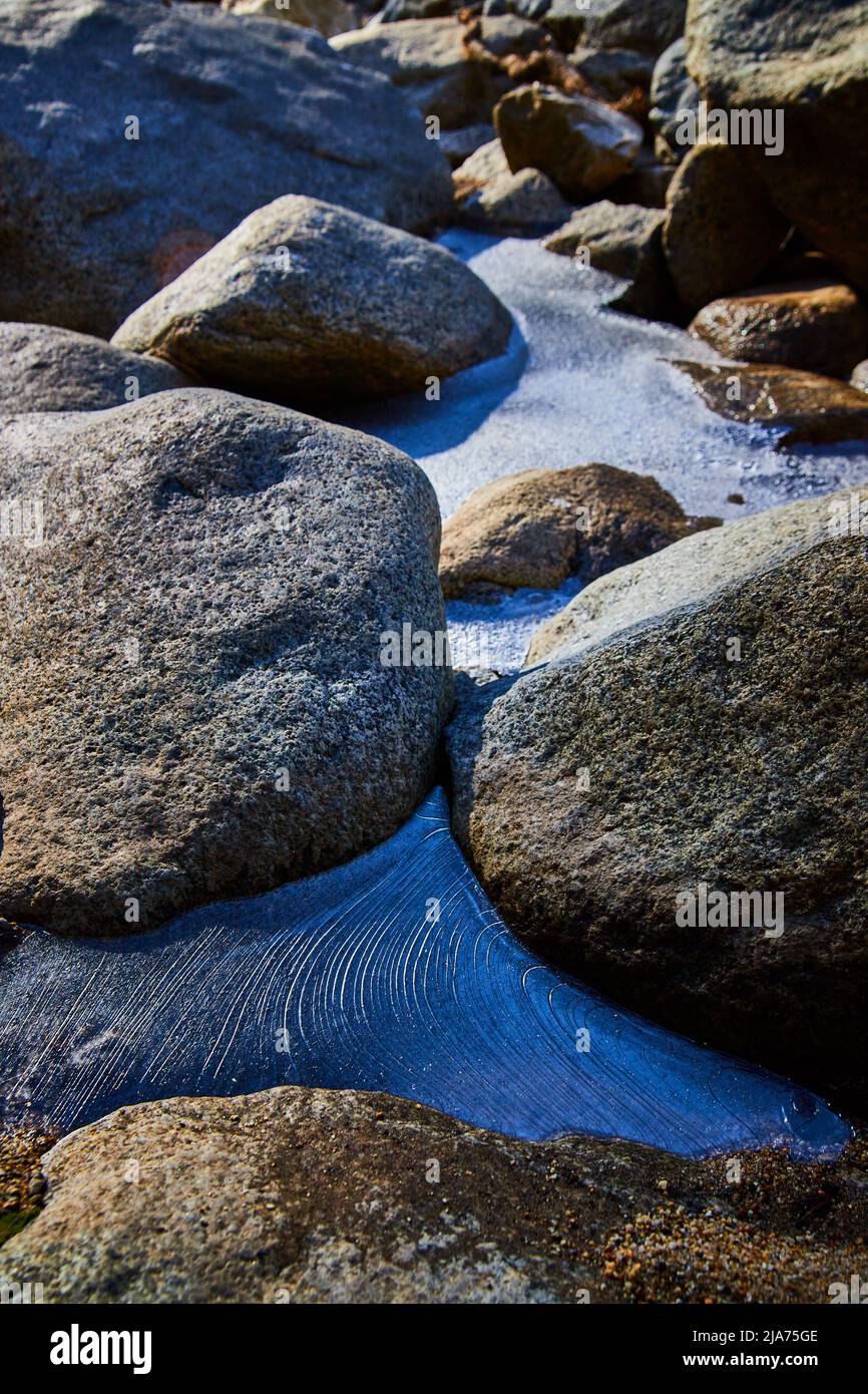 Dettaglio di un motivo di ghiaccio congelato ondulato tra le rocce Foto Stock