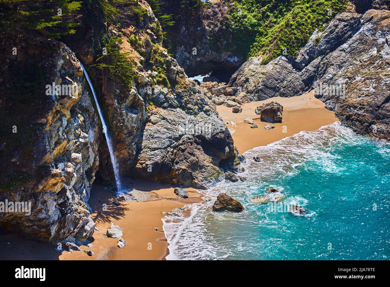 Rocce costiere con cascata che si stende sulle spiagge sabbiose accanto alla baia dell'oceano Foto Stock