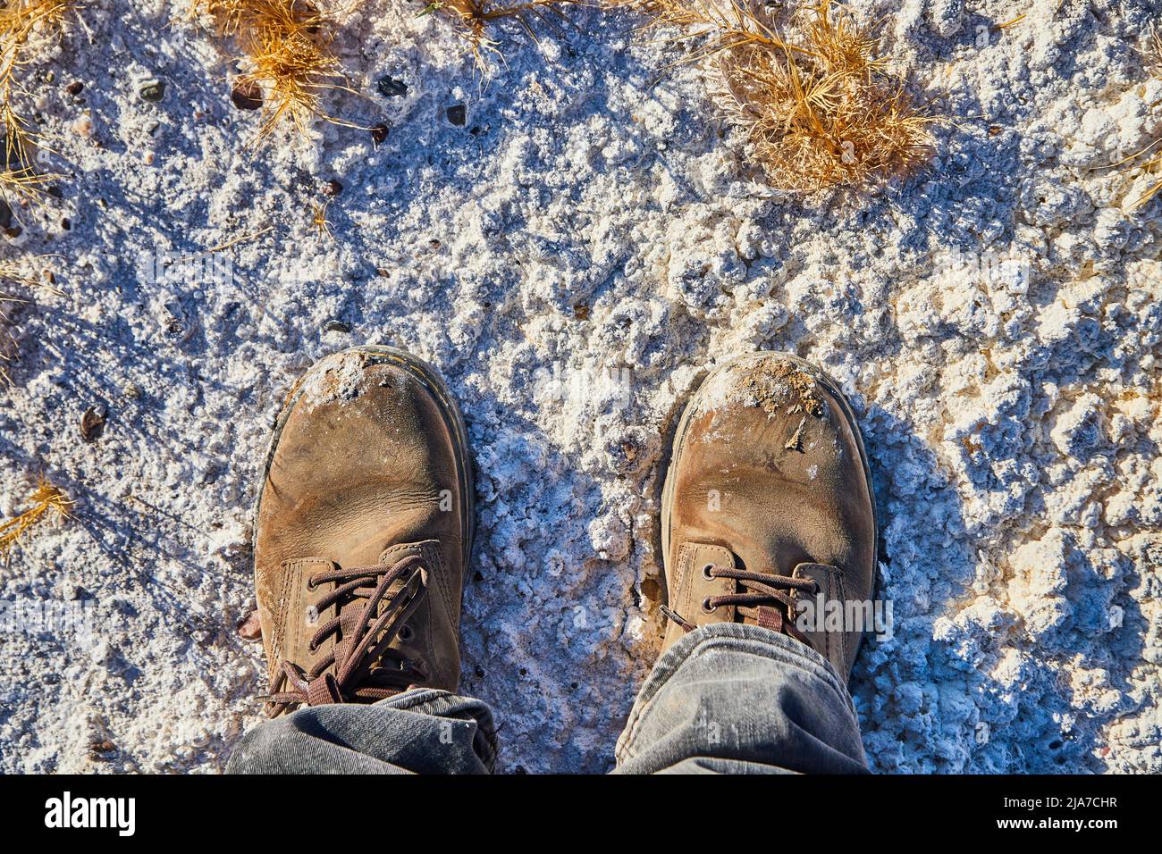 Stivali in piedi nel deserto di sabbia bianca polverizzata con erbe gialle Foto Stock