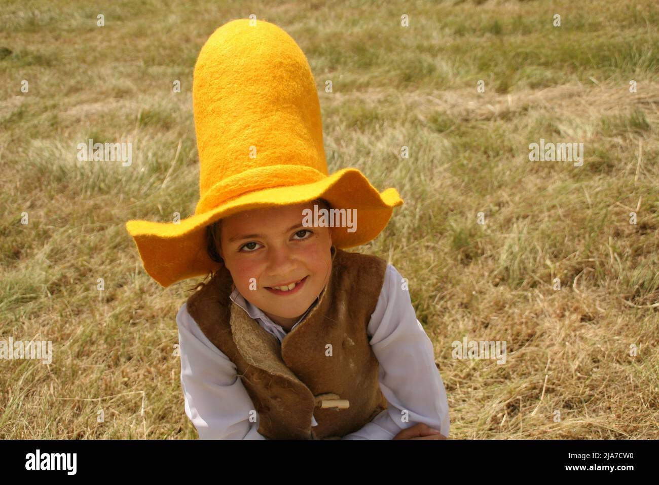 Ragazza in un cappello di agricoltore giallo alto con l'orlo largo sta camminando nel campo verde in estate. Ha un lungo capelli marroni, una sola treccia è appesa giù Foto Stock