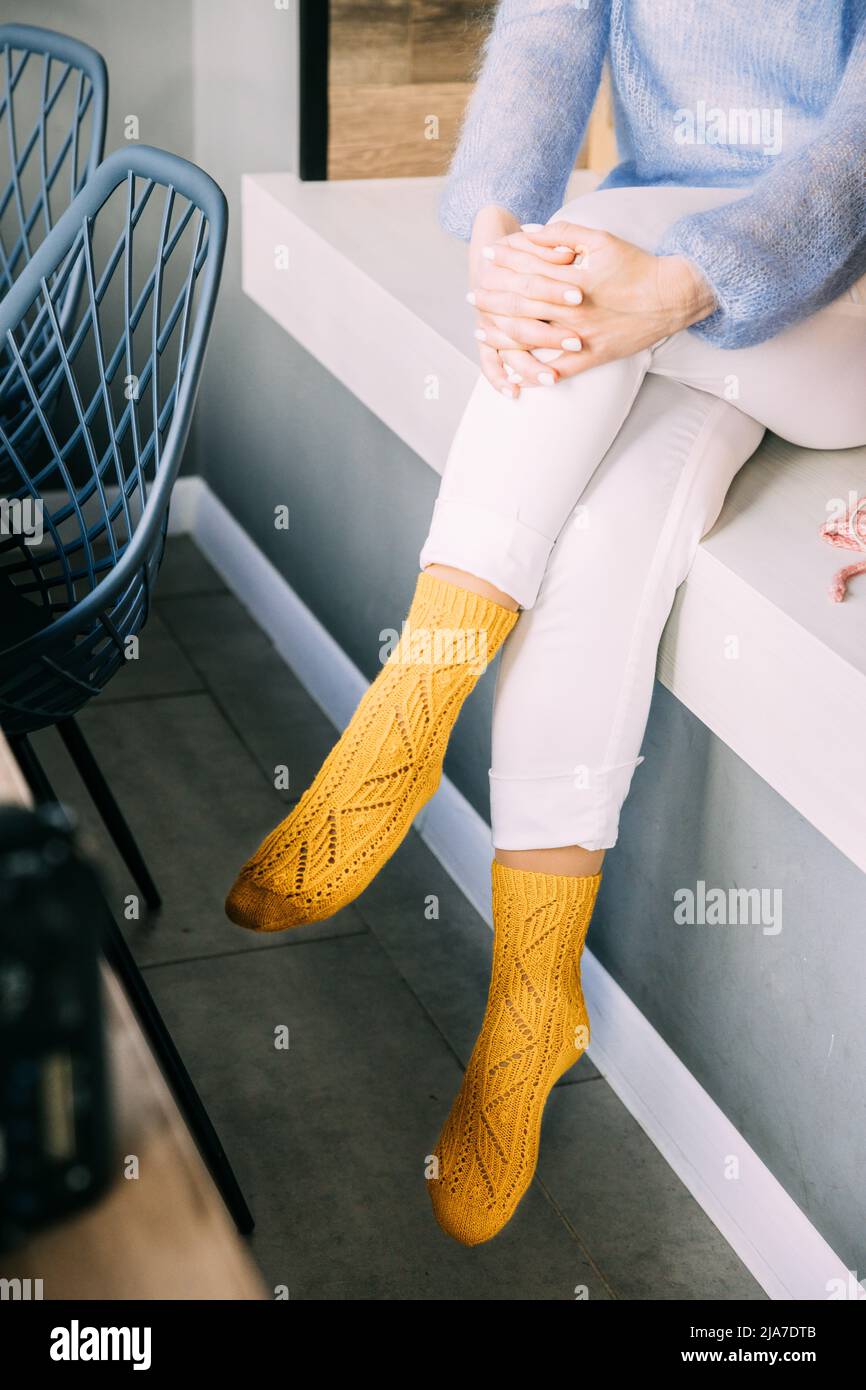 Donna confortevole in maglia di lana giallo d'inverno calzini, pantaloni bianchi e blu caldo maglione che riposa su una panca al caffè in inverno Foto Stock