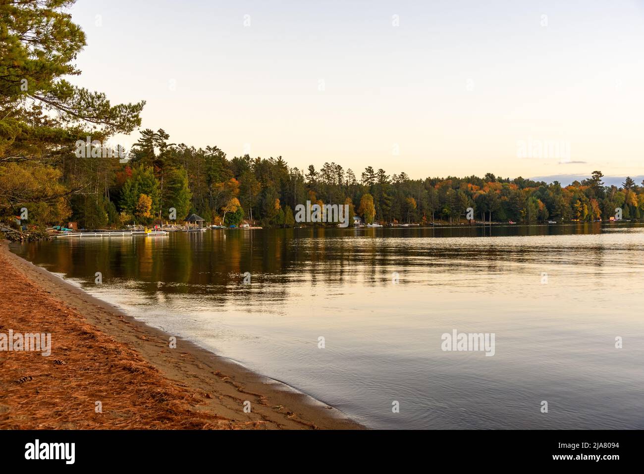 Molo di legno lungo le rive boschive del lago al crepuscolo in autunno. Scena tranquilla. Foto Stock