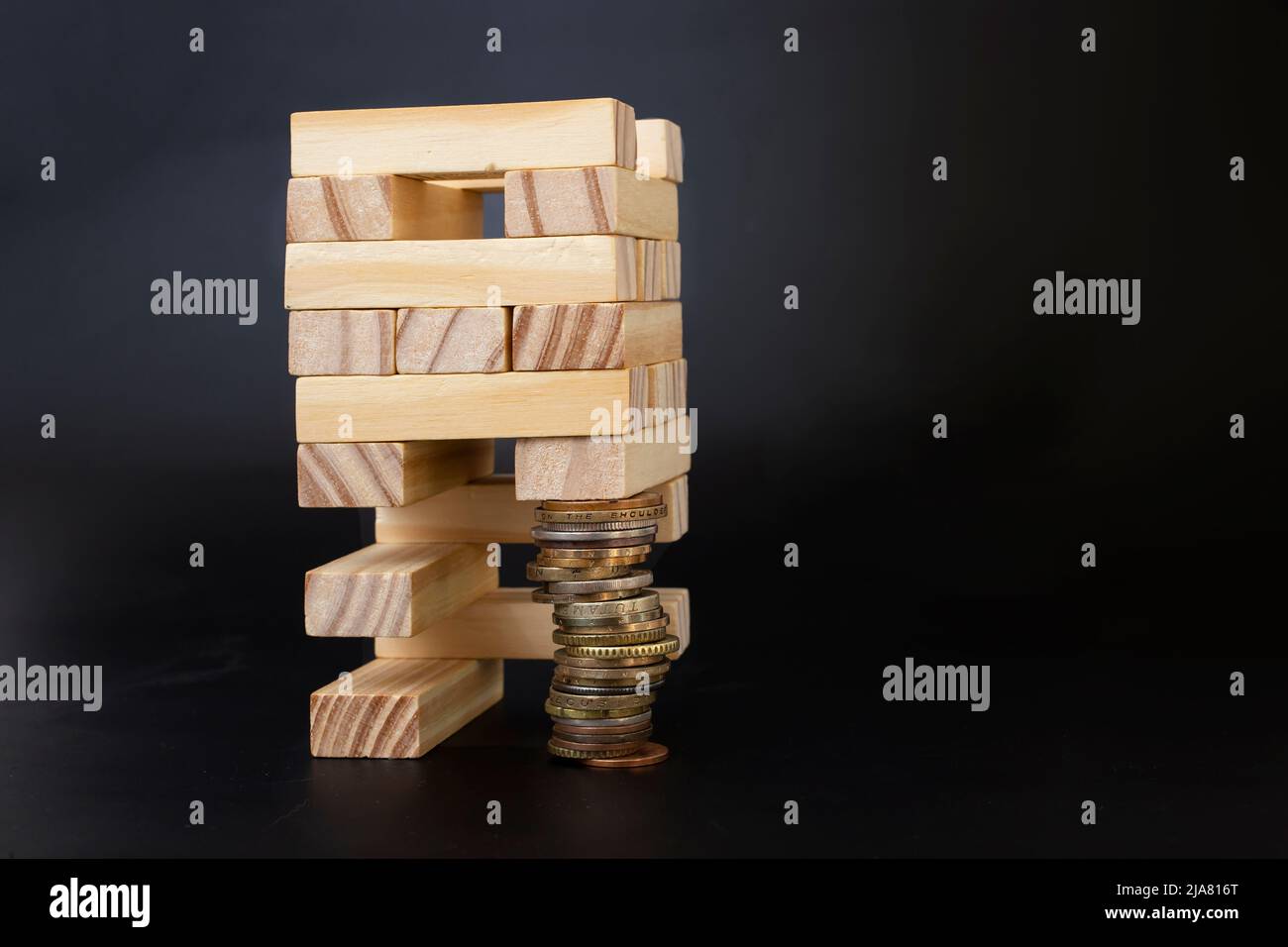 struttura di blocchi di legno supportata da una pila di monete. Costruzione gioco metafore isolato su sfondo nero. Foto Stock