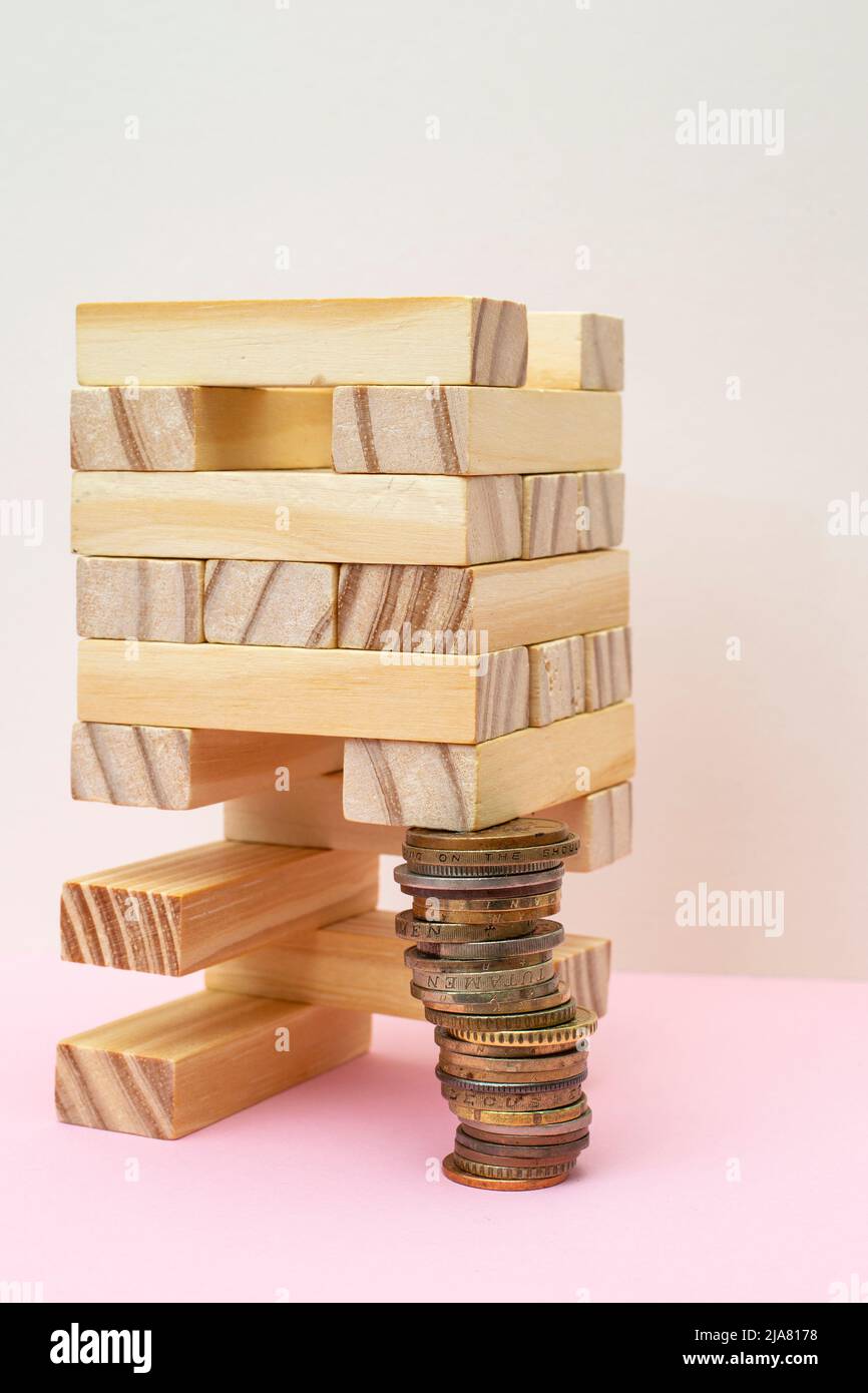 struttura di blocchi di legno supportata da una pila di monete. Metaphor gioco di costruzione su sfondo rosa. Foto Stock