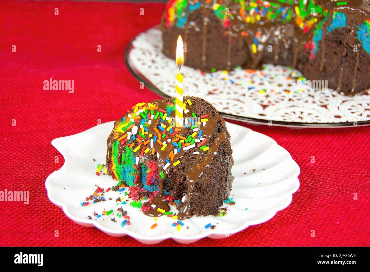 Candela di compleanno in una fetta di torta al cioccolato arcobaleno Foto Stock