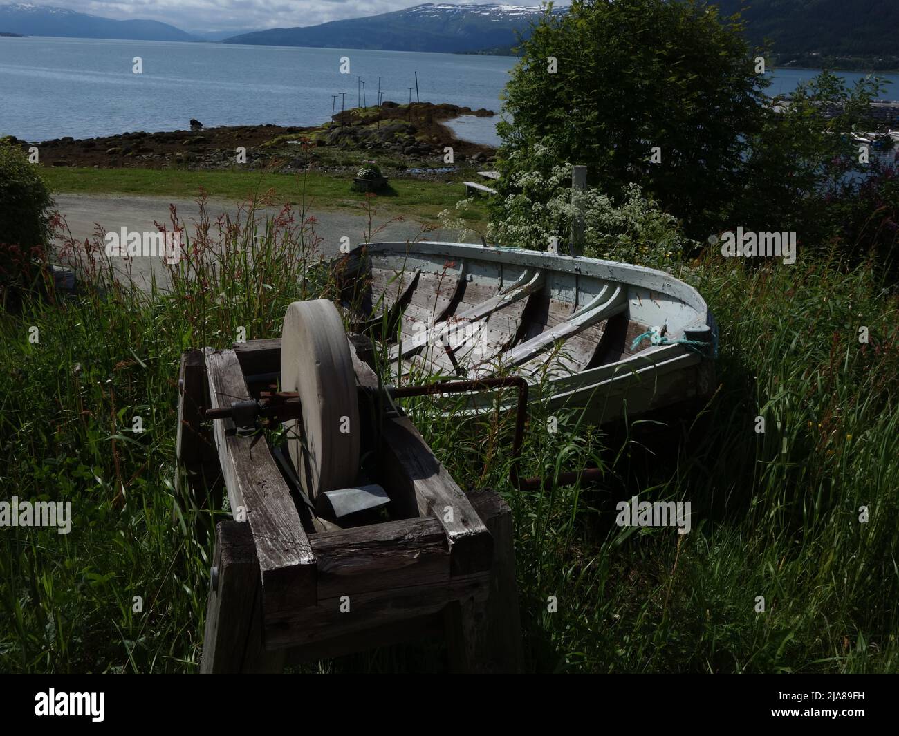 Un'antica pietra arenaria e una barca a remi si trovano in profondità nell'erba all'estremità di Moholmen. MO i Rana, Norvegia. Foto Stock