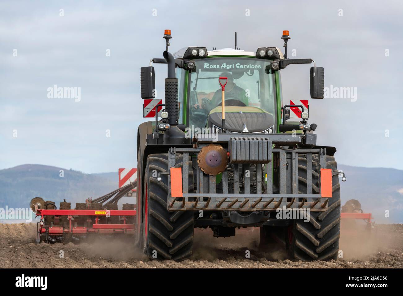 Una vista frontale di un coltivatore in un trattore Fendt che tira una seminatrice a disco in un campo in primavera Foto Stock