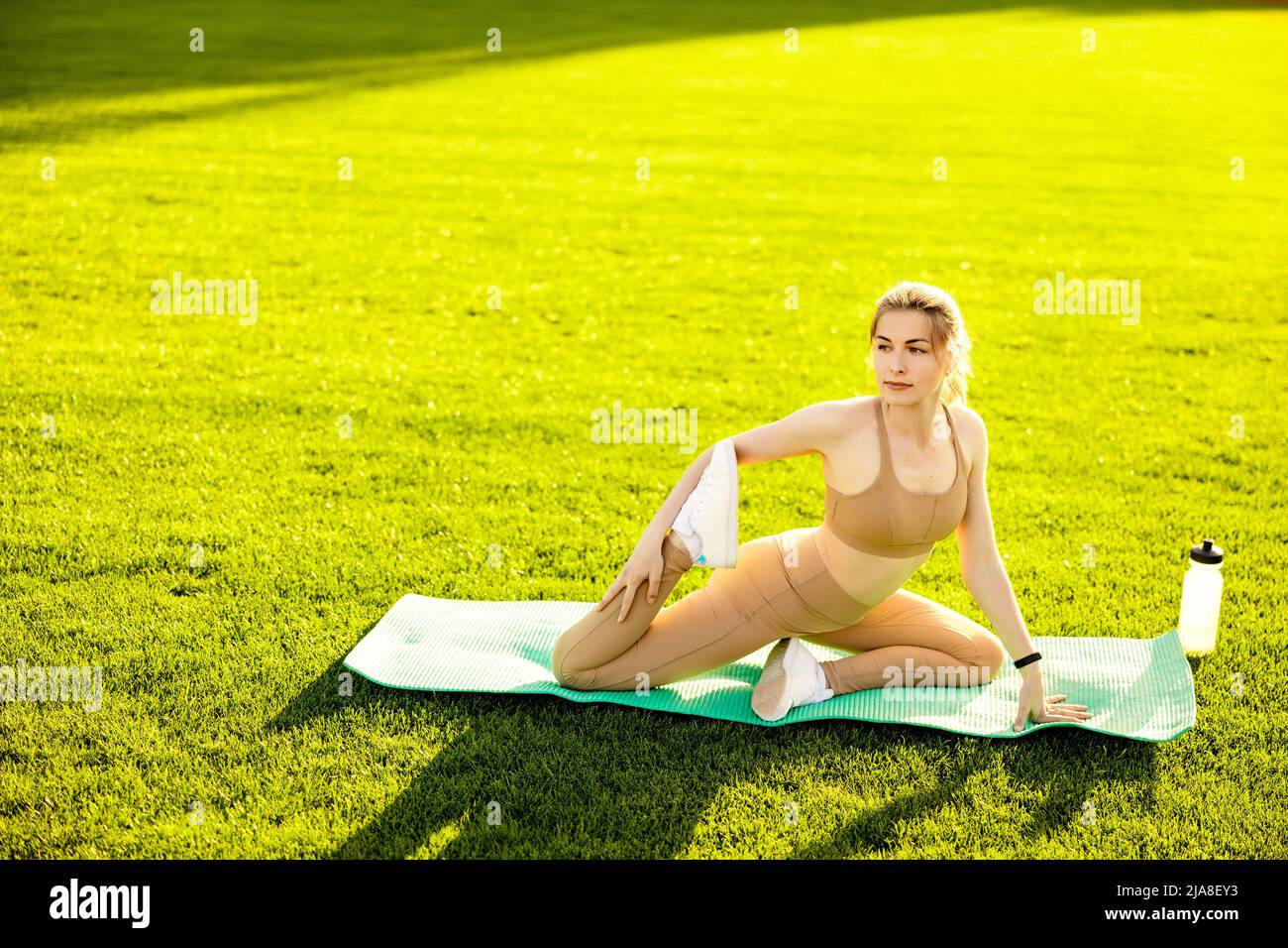 Bella donna sportiva che fa stretching allo stadio, pratica flessibilità, atletica formazione donna in posa relax, raccomandato stile di vita sano Foto Stock