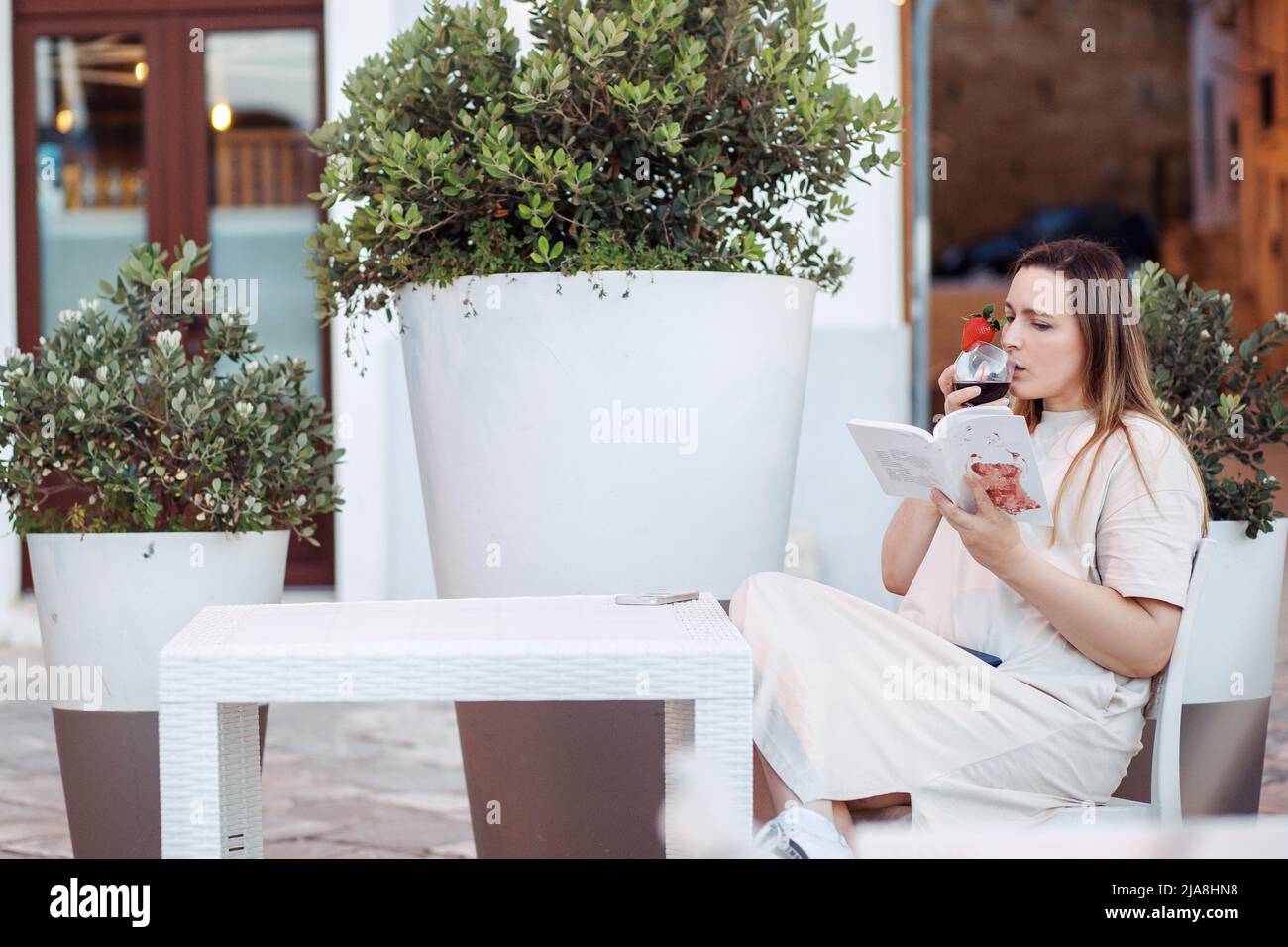 Elegante e affascinante donna bionda lettura eccitante libro bere alcol sedersi al tavolo in caffetteria all'aperto. Weekend di vacanza Foto Stock