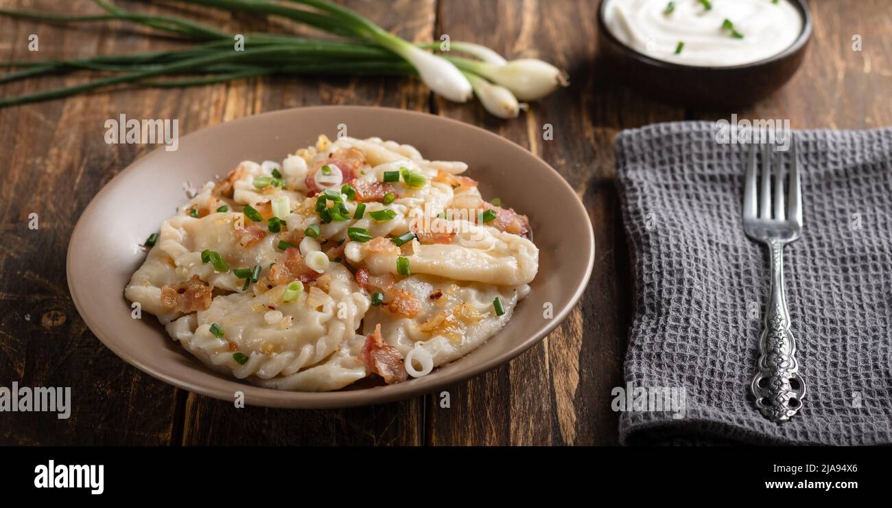 Gnocchi di patate con panna acida sul tavolo di legno. Cibo tradizionale ucraino. Varenyky, vareniki, pierogi, pirohi - gnocchi con ripieno. Foto Stock