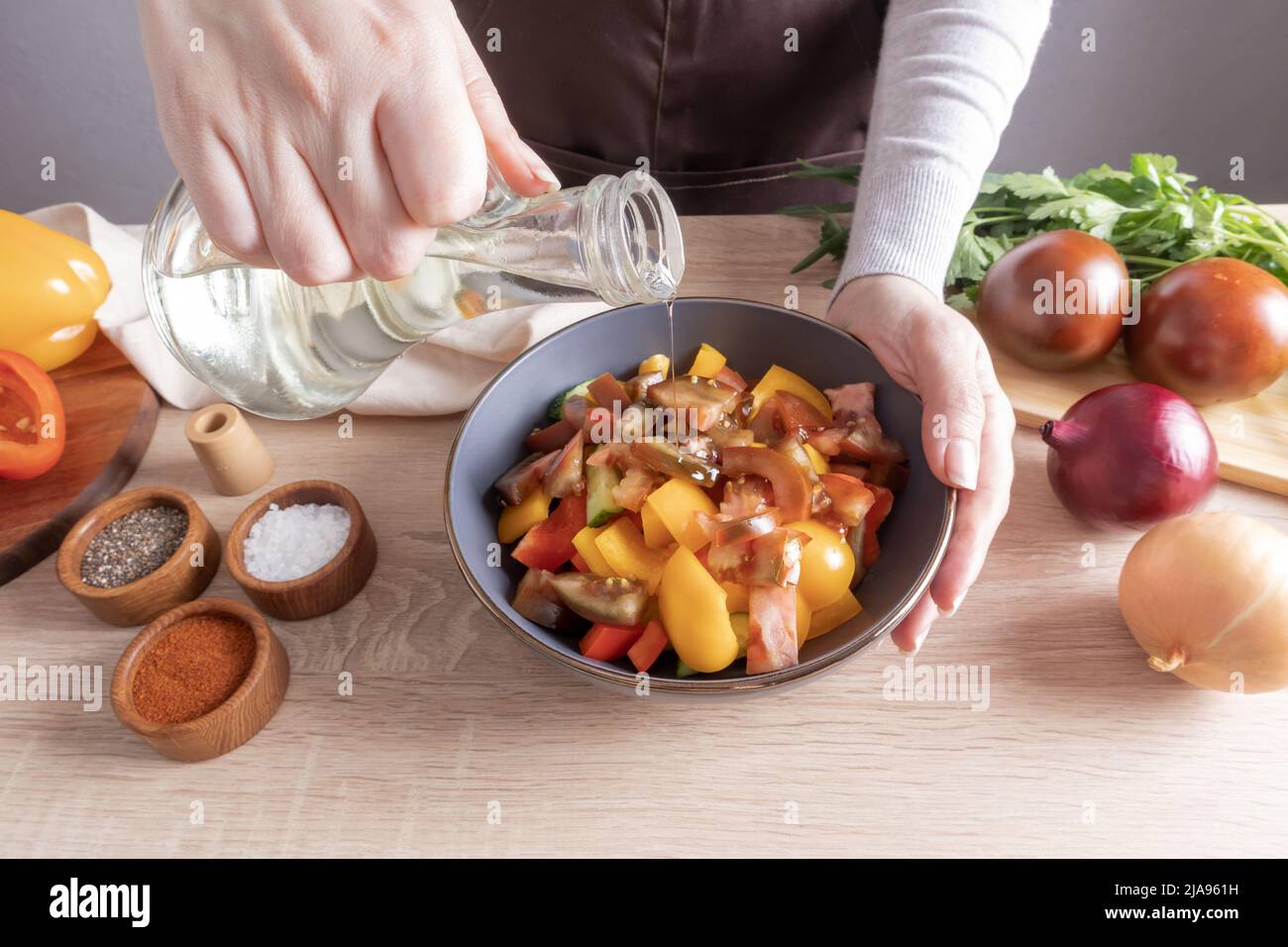 la mano di una bambina versa l'olio da una bottiglia sopra la lattuga tagliata a fette in una ciotola. cucinando a casa Foto Stock