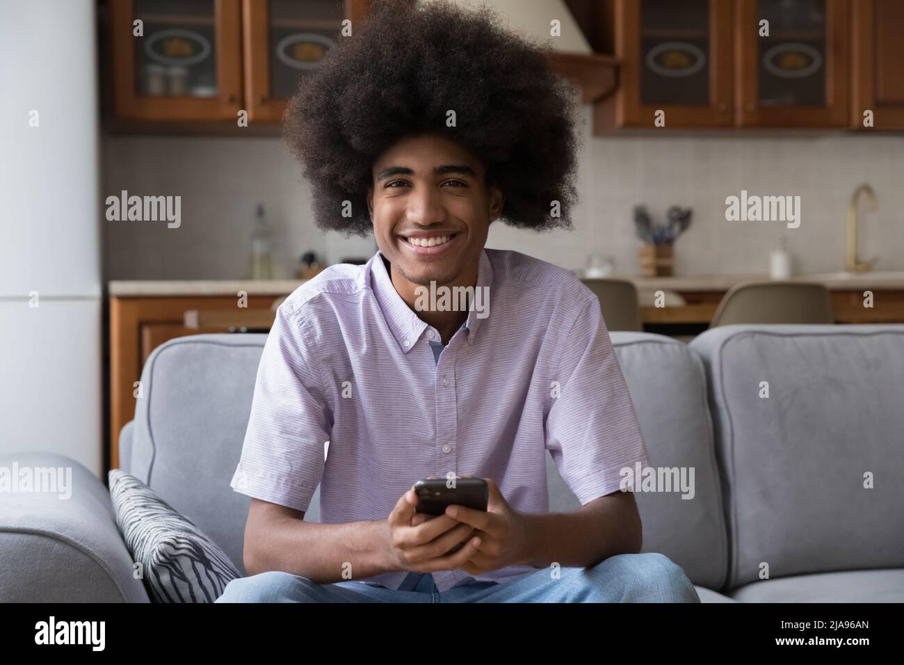 Ragazzo felice con capelli ricci lunghi e sfocati utilizzando lo smartphone Foto Stock