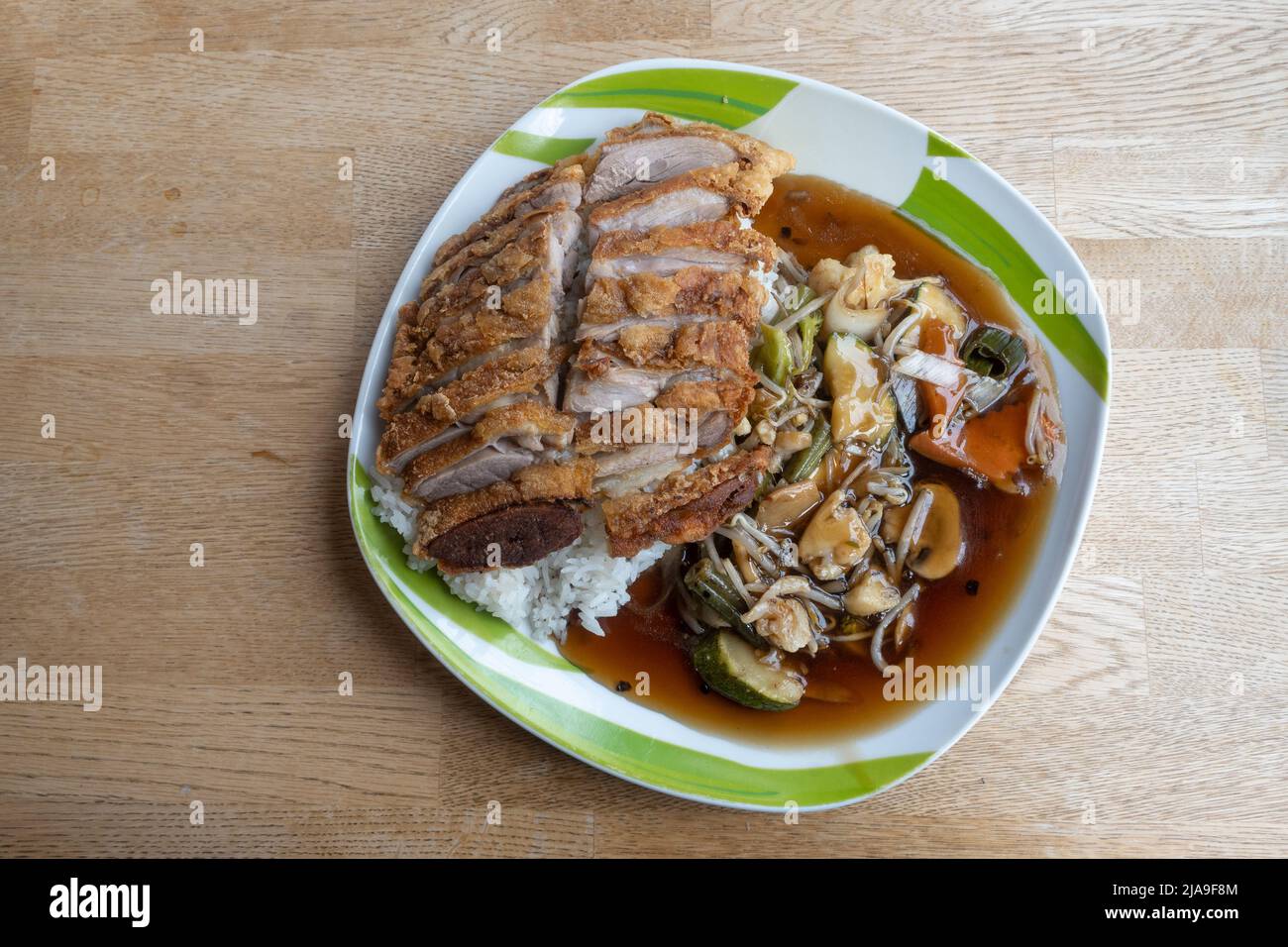 Piatto cinese di carne di anatra fritta croccante su riso con verdure e salsa su un piatto e un tavolo di legno, spazio copia, alto angolo di vista dall'alto, sele Foto Stock