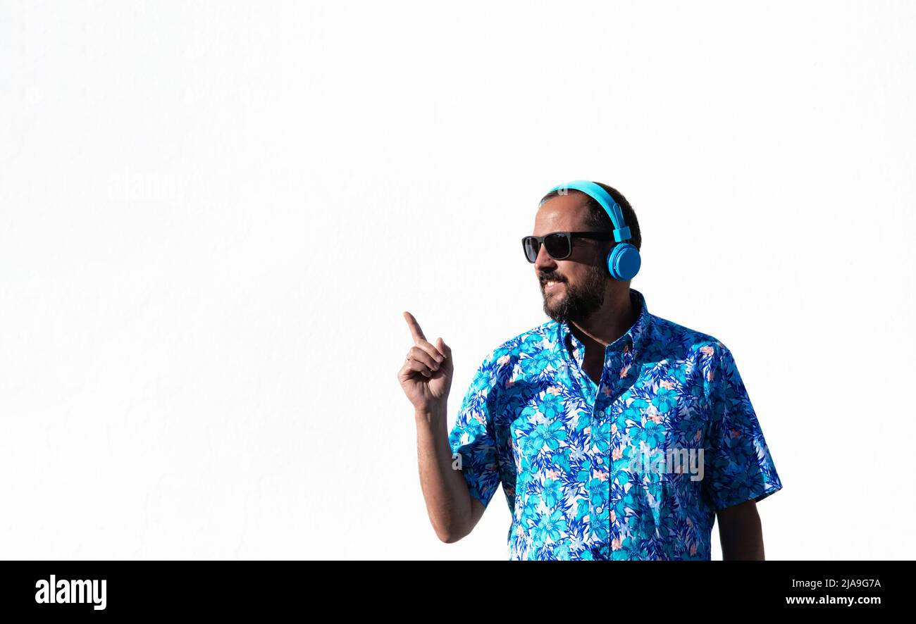 giovane uomo hipster con barba, occhiali da sole, maglietta hawaiana e cuffie blu che sorridono con le dita verso l'alto. spazio copia. sfondo bianco Foto Stock
