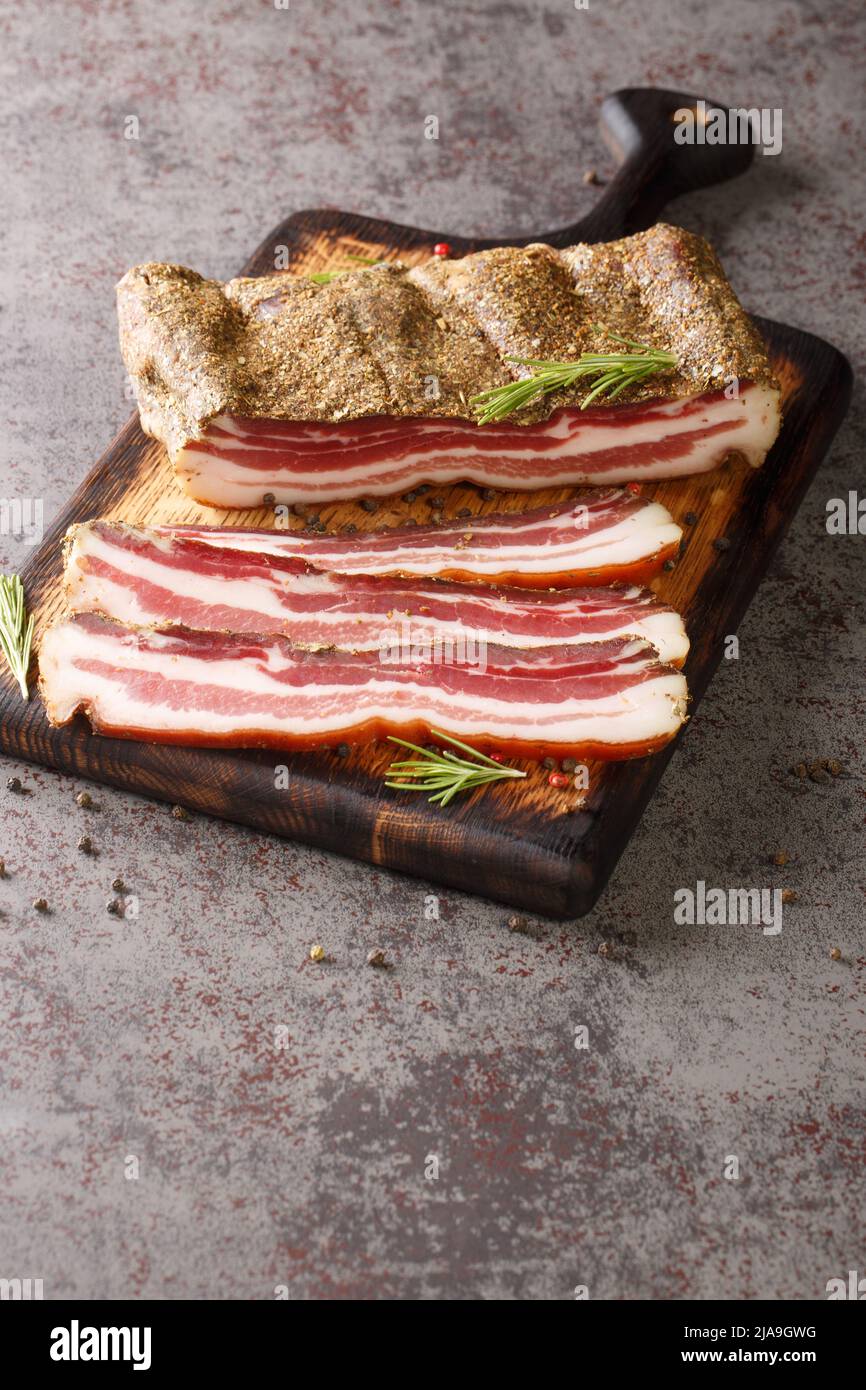 Pezzi freschi di pancia di maiale crudo in un contenitore monouso di  plastica trasparente cibo vicino a tagliere di legno e coltello affilato  sul tavolo da cucina. Cucinare a casa Foto stock 