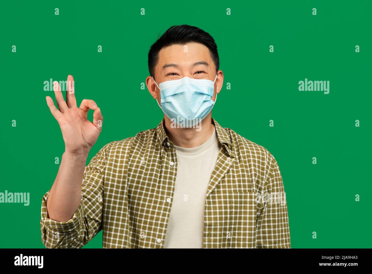 Felice uomo asiatico maturo in maschera medica volto mostrando un gesto OK, raccomandando la protezione durante la pandemia globale Foto Stock