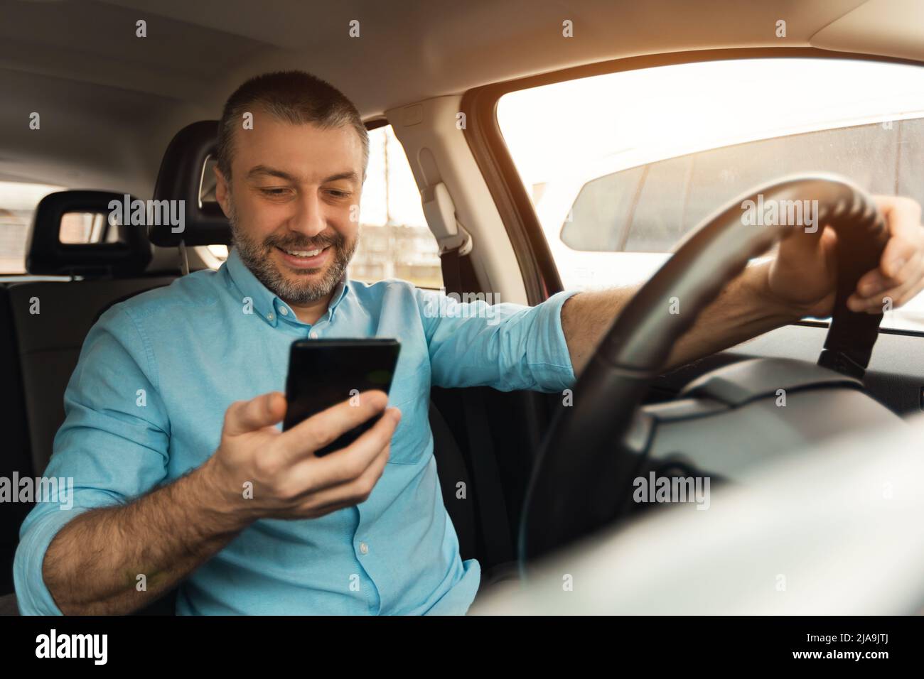 Uomo felice che usa lo smartphone durante la guida dell'auto Foto Stock