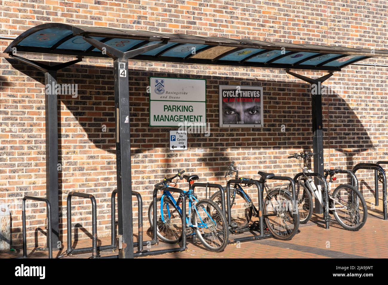 Un rifugio per biciclette Basingstoke council con un portabiciclette e biciclette e un poster di avvertimento "i ladri della bicicletta ti stiamo guardando" con un paio di occhi. REGNO UNITO Foto Stock