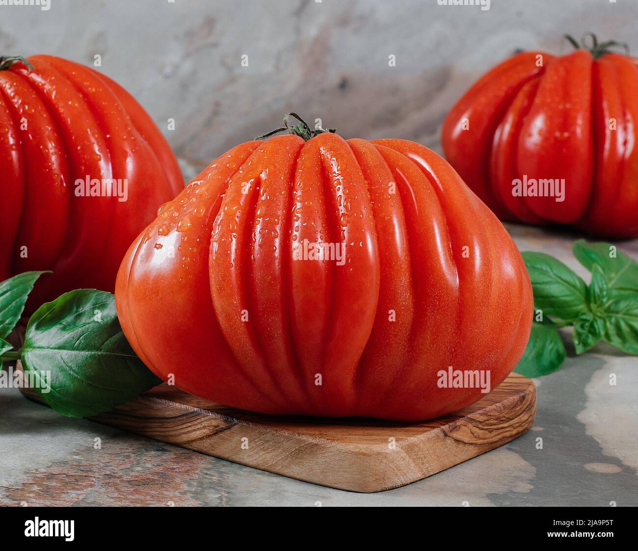 Fresco Raf Coeur De Boeuf pomodori e basilico su uno sfondo marrone, concetto rustico, foto di scorta Foto Stock