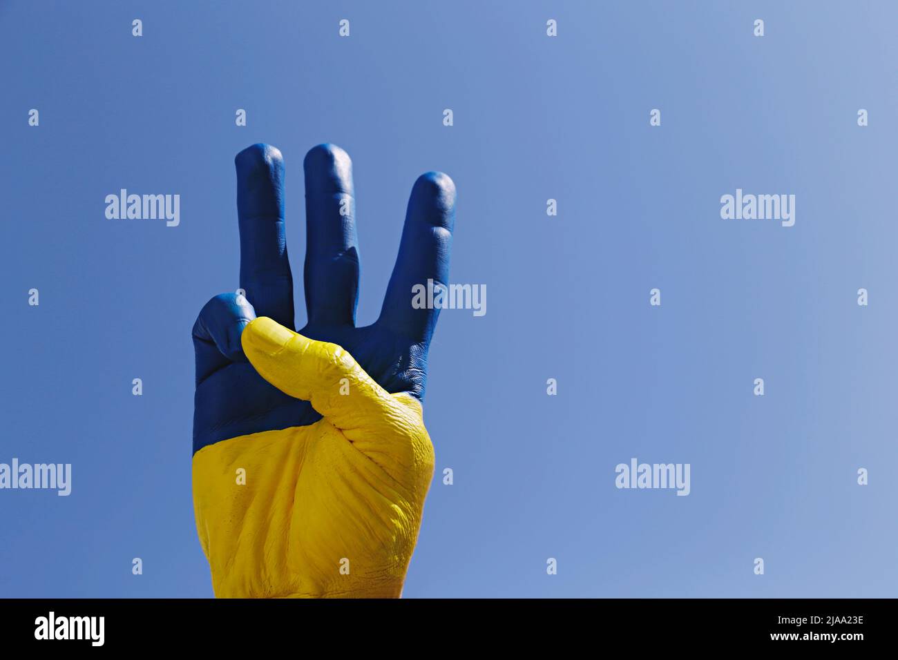 Mano dell'uomo illuminata dal sole dipinta nei colori della bandiera nazionale Ucraina che mostra un tradizionale gesto di mano tridente come simbolo di sostegno e solidari Foto Stock