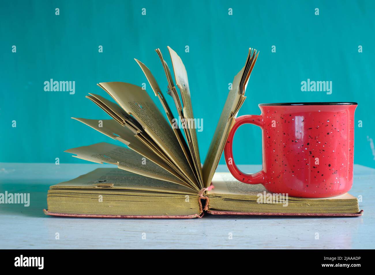 Libro aperto, libro vintage hardback e vecchia tazza di caffè su sfondo teal. Educazione, lettura, concetto di ricerca. Foto Stock