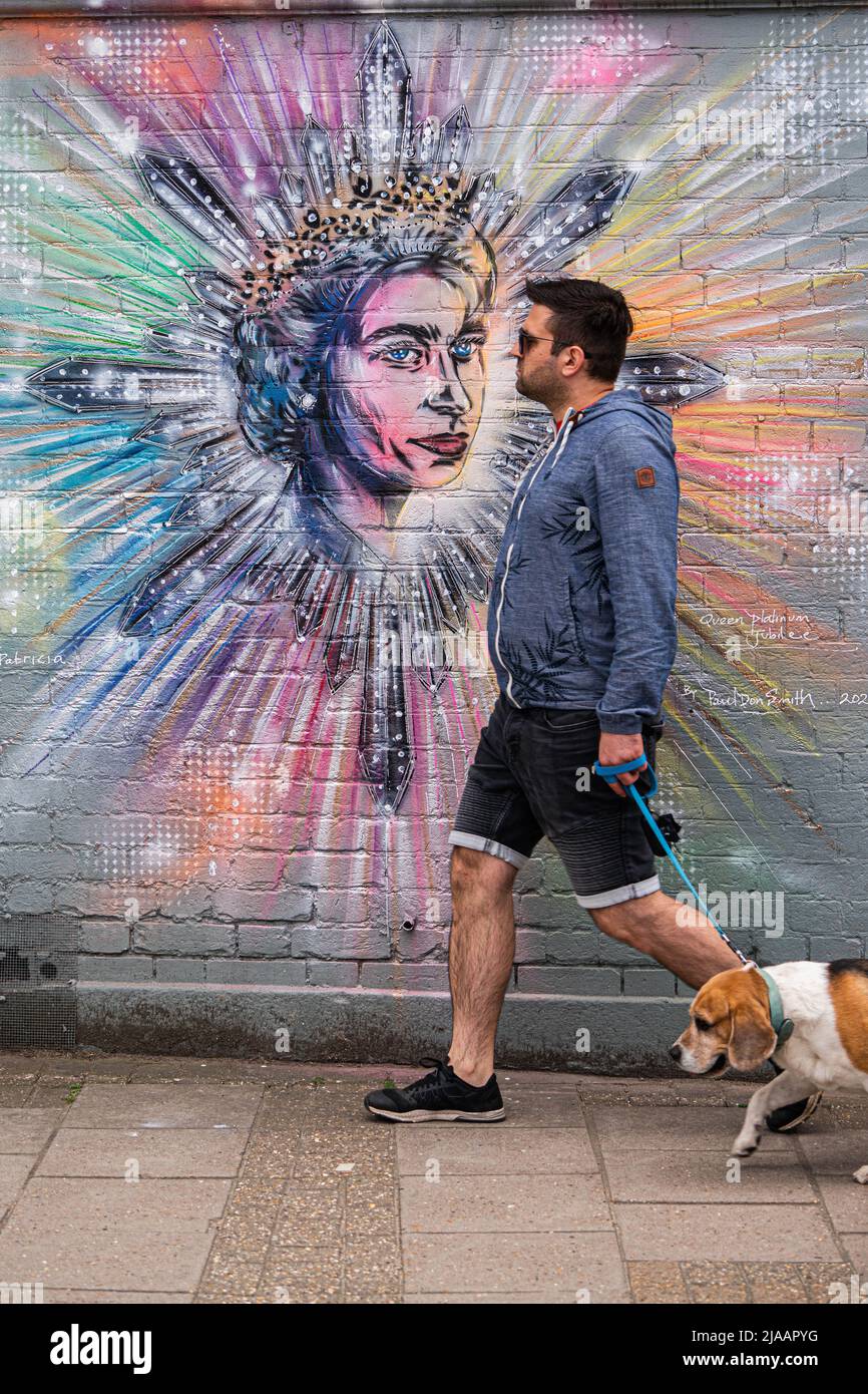 Londra UK, 29 maggio 2022. Un uomo cammina il suo cane davanti ad un murale a Wimbledon dell'artista Paul Don Smith dedicato al giubileo di platino della regina Elisabetta II . Credit. amer Ghazzal/Alamy Live News Foto Stock