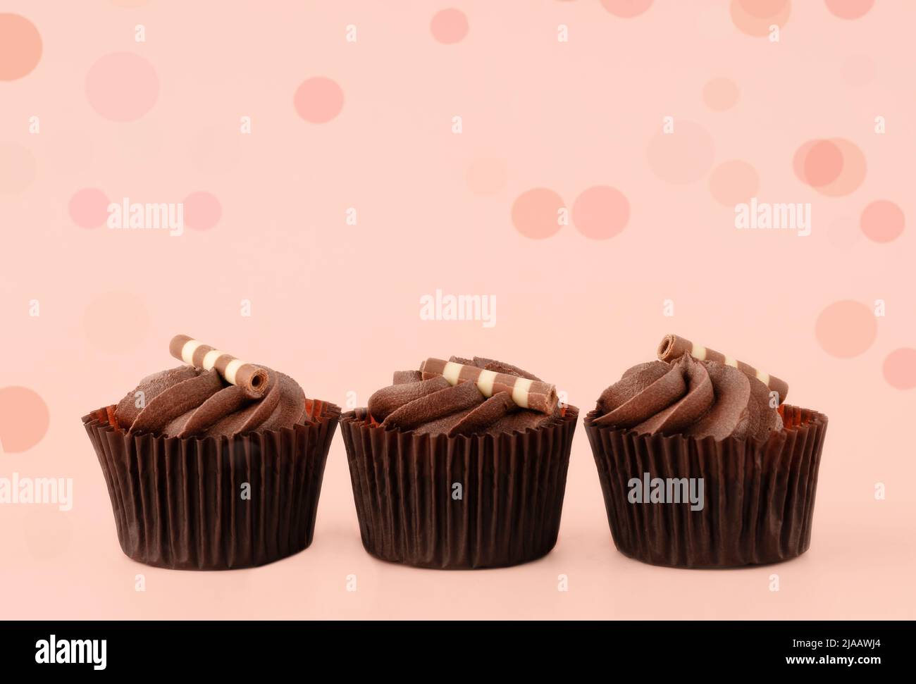 muffin al cioccolato in crema in involucri marroni su sfondo rosa foto di alta qualità per calendario e carte. Spazio per il testo Foto Stock