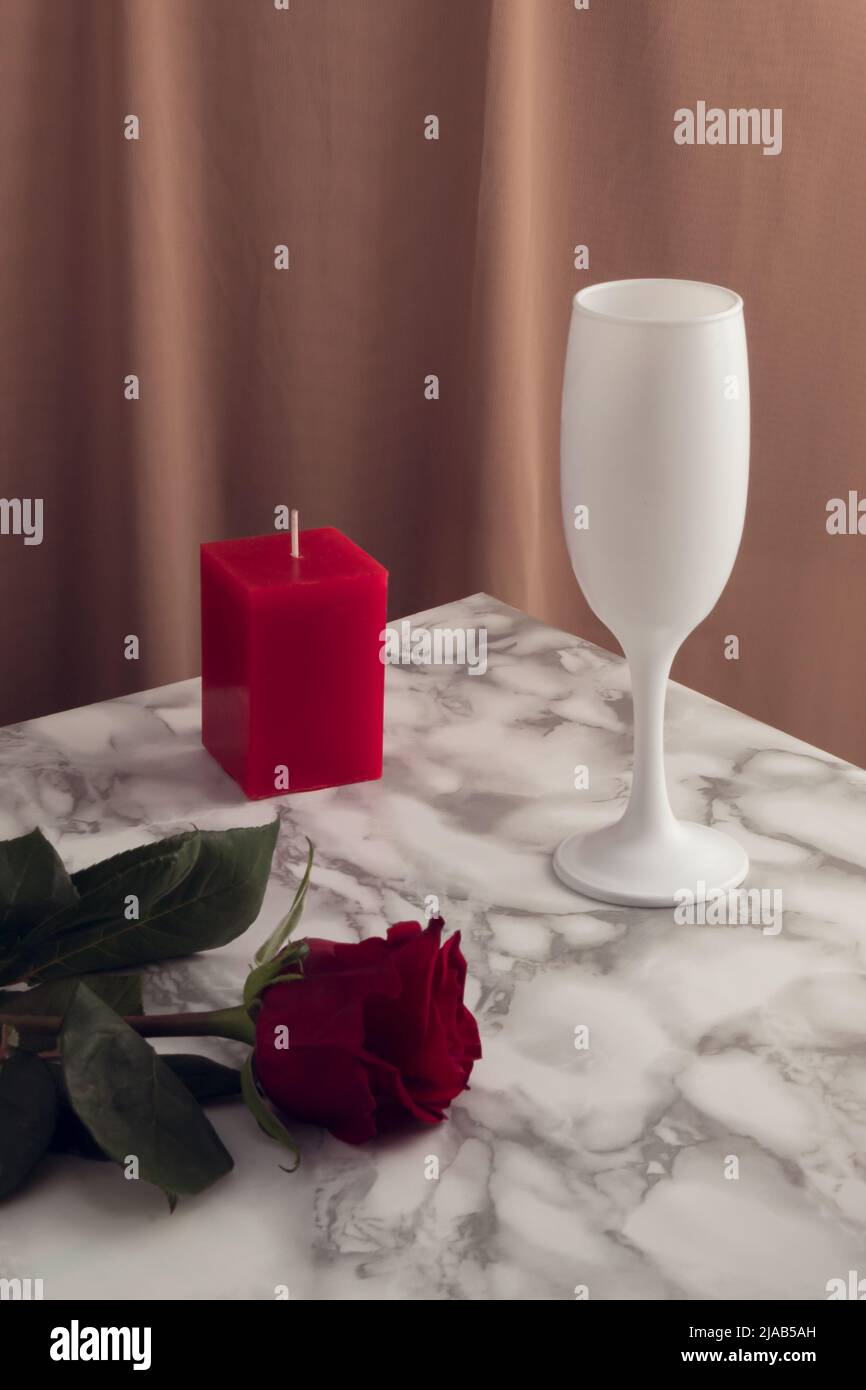 Concetto di stile vintage con bicchiere da vino, candela e fiore rosso rosa su tavolo in marmo. Festa di San Valentino retrò concetto. Estetica moderna. Foto Stock