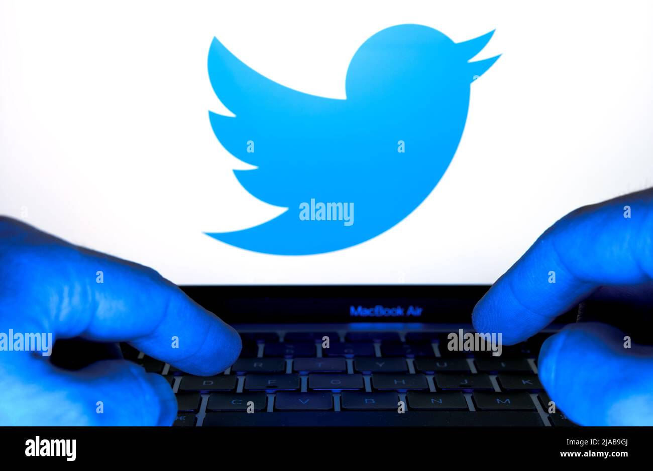 Digitazione delle mani su una tastiera illuminata da una luce blu. Notebook con logo Twitter sfocato. Concetto. Stafford, Regno Unito, 29 maggio 2022 Foto Stock