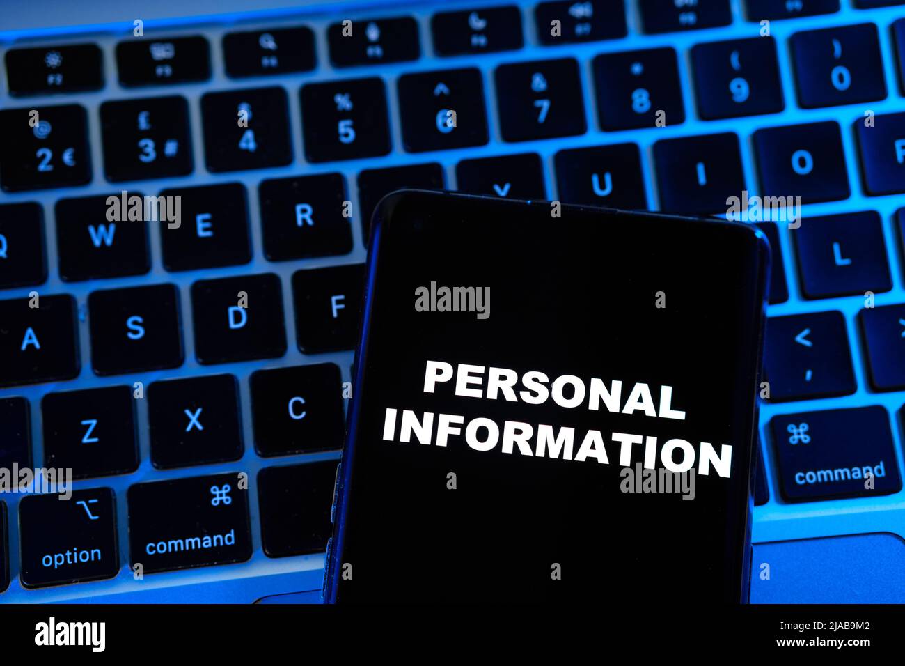 Frase DI INFORMAZIONI PERSONALI visualizzata su uno smartphone posizionato su un notebook sfocato con luce blu dietro di esso. Concetto. Foto Stock
