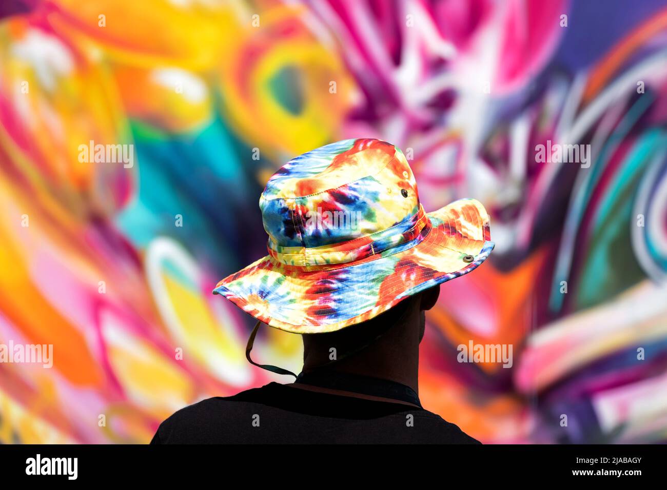 Bristol, Regno Unito. 28th maggio 2022. Un artista di strada che indossa un colorato cappello tinto legato si erge indietro per vedere la sua opera d'arte durante il festival Bristol Upfest Foto Stock