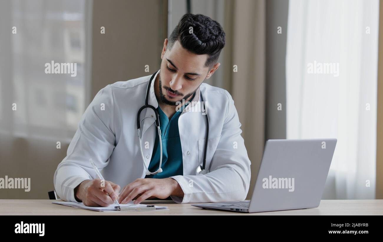 Uomo arabo concentrato medico professionista siediti al gabinetto clinica uso computer chatting distante in medico sociale app dare consultazione online Foto Stock