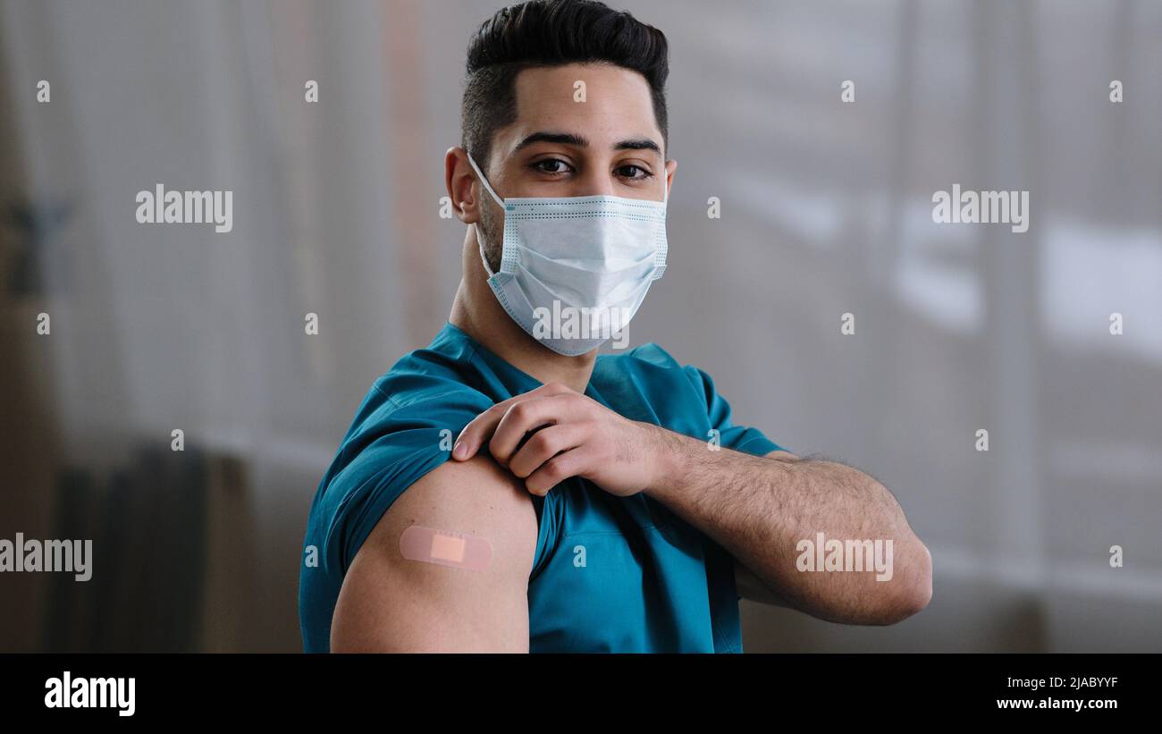 Inspirato uomo ispanico arabo giovane medico infermiere intern medico maschera che mostra iniezione marchio adesivo spalla fare vaccino Foto Stock