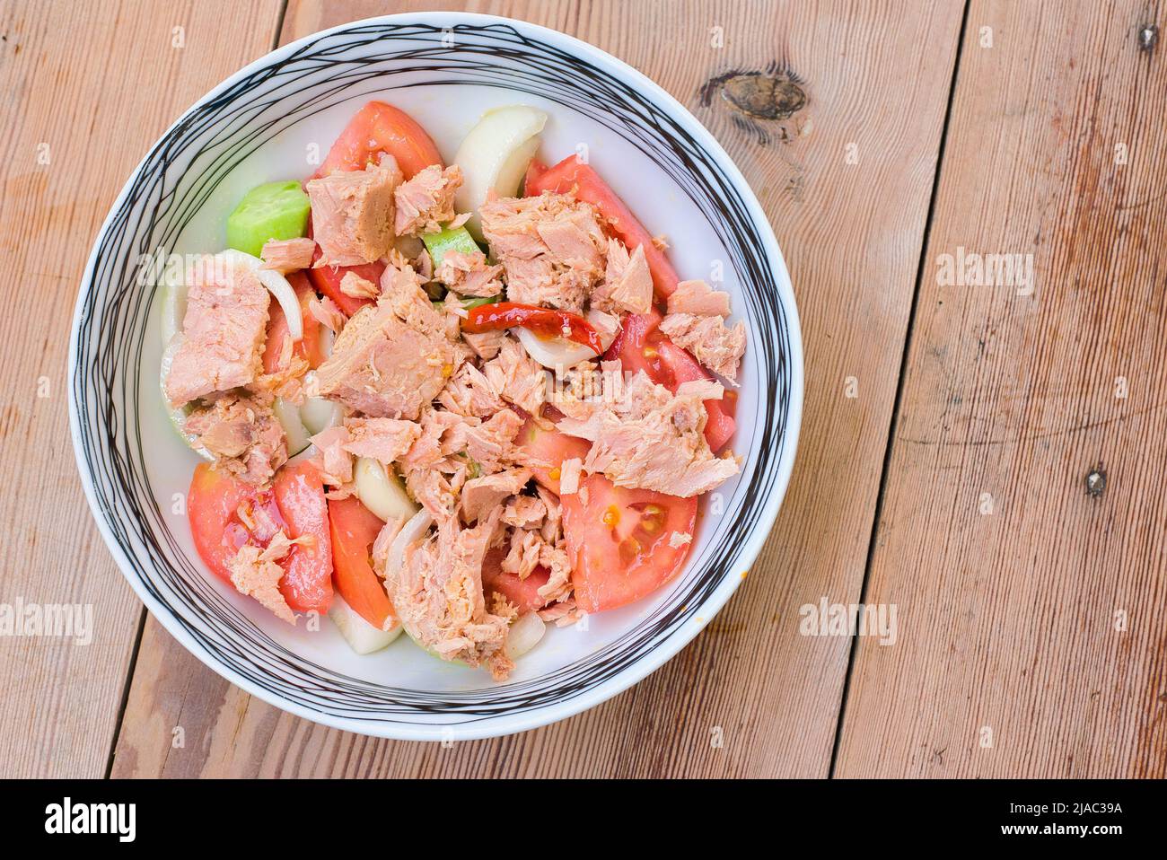 Ciotola di pomodoro crudo con olio d'oliva, cetriolo, cipolla, tonno, su tavola di legno Foto Stock