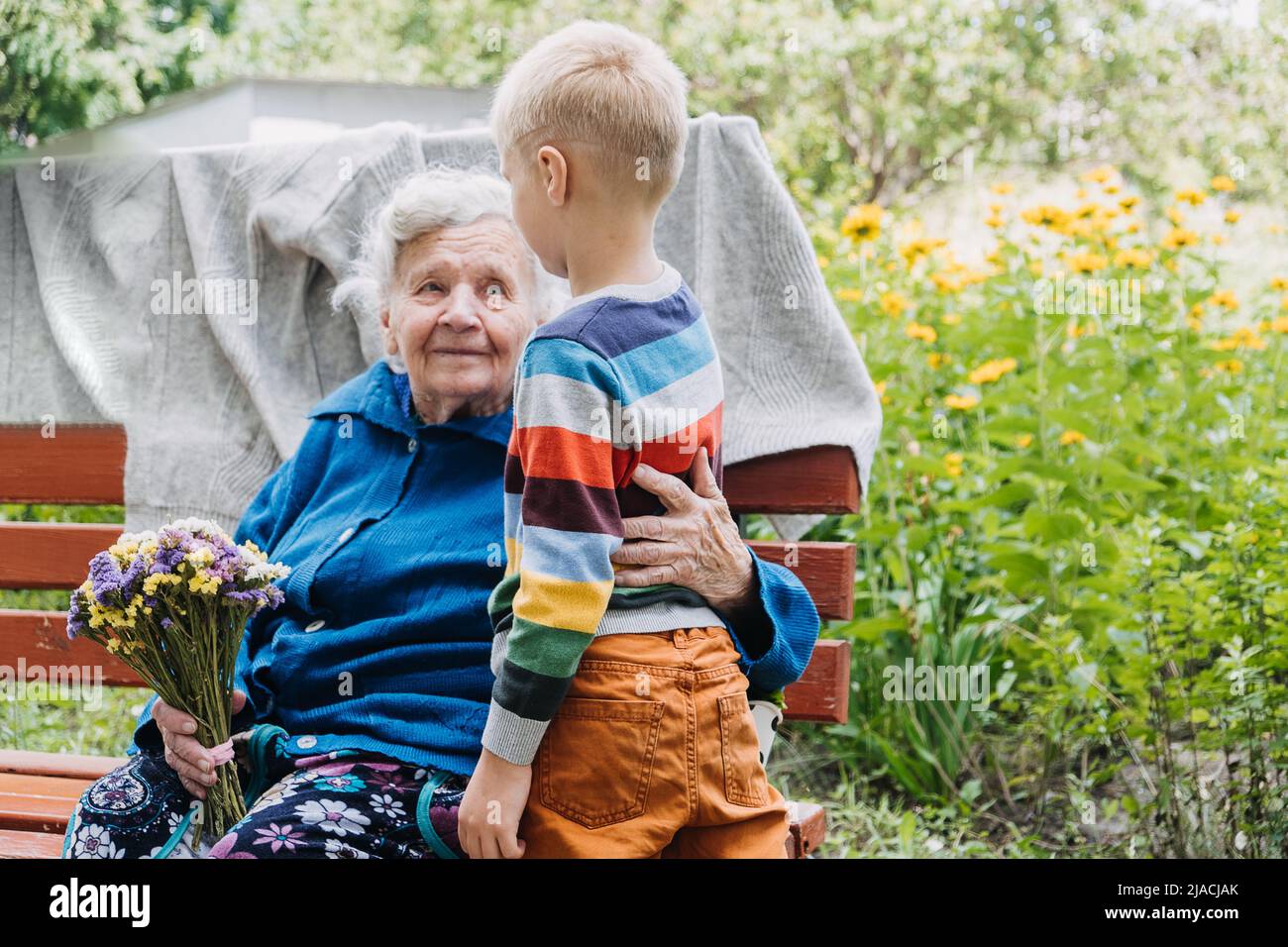 Nipote ragazzo che dà un fiore alla nonna. Nonna e nipote trascorrono del tempo insieme. Granny con i nipoti che si divertono insieme all'aperto Foto Stock