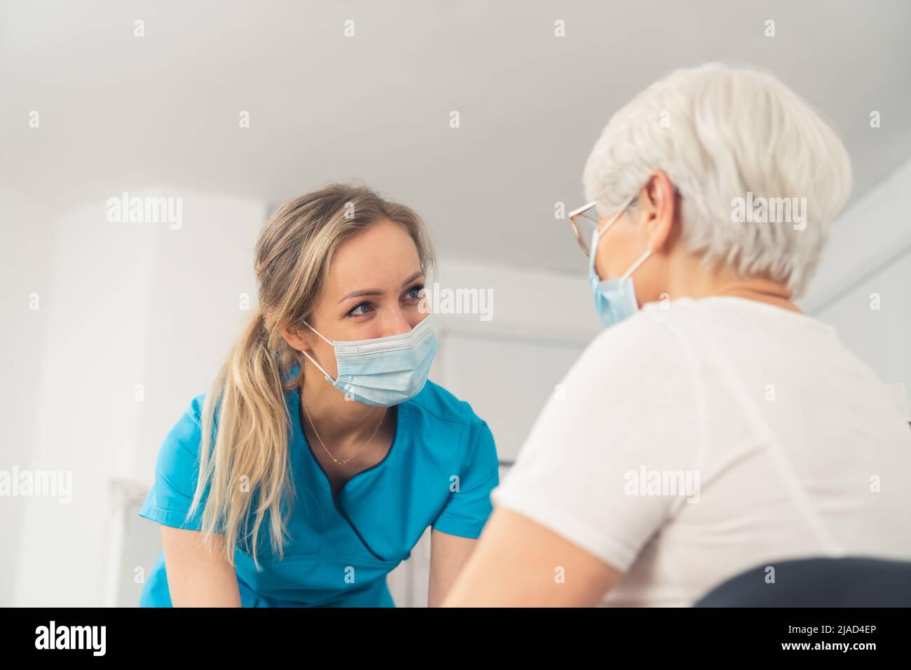 Giovane infermiere caucasico donna che aiuta e guarda una donna anziana, entrambi stanno indossando le maschere. Concetto Helthcare. Scatto interno. Foto di alta qualità Foto Stock