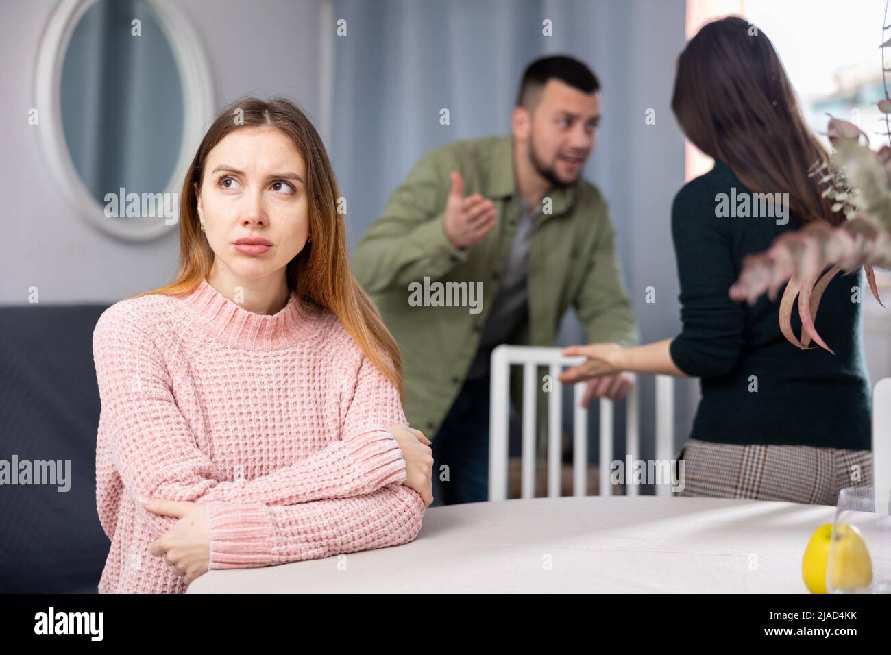 Donna triste seduta a tavola a casa mentre la gente litigava Foto Stock