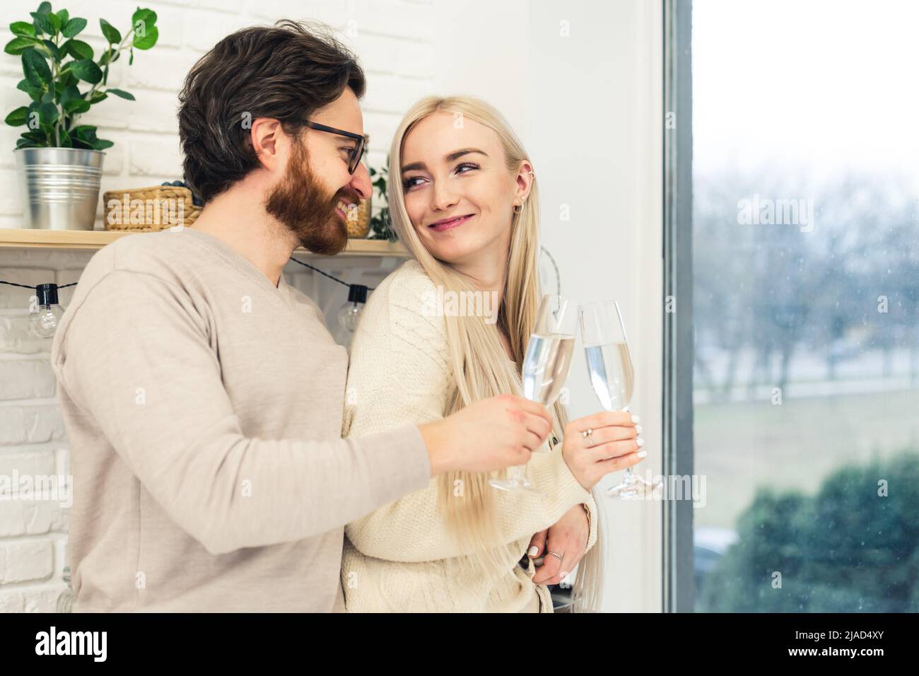 Scatto interno in una cucina di attraente giovane coppia caucasica che tiene i vetri del vino che si guardano con affetto. Concetto di celebrazione. Foto di alta qualità Foto Stock