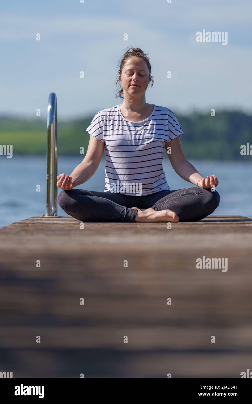 Donna seduta a gambe incrociate su un molo meditating, Wallersee, Salisburgo, Austria Foto Stock