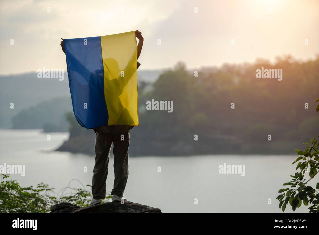 Vista posteriore di una donna in piedi da un fiume che tiene una bandiera Ucraina sopra la sua testa, Thailandia Foto Stock