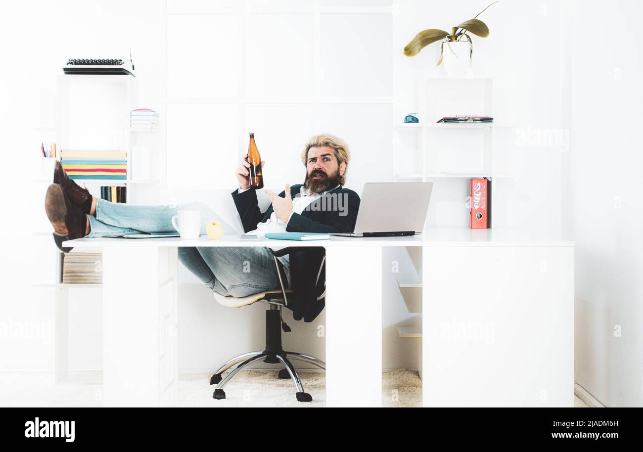 Uomo d'affari stanco annoiato che brilica sul posto di lavoro vicino al laptop, lavoro noioso, lavoro di fine lavoro morto, overwork extra dopo l'orario di lavoro, bere alcol. Foto Stock